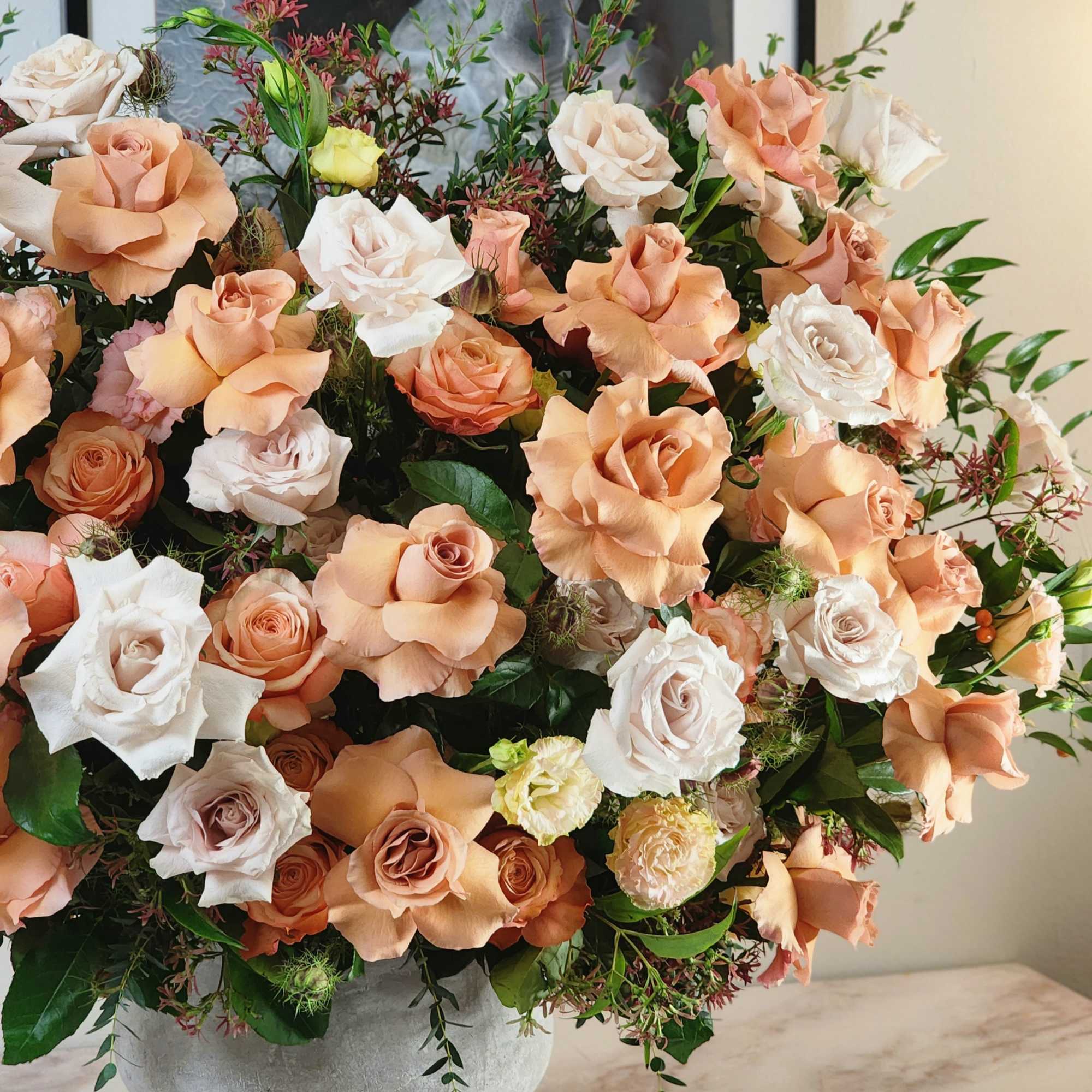 A grandiose vase holds an enchanting blend of beige and peach roses