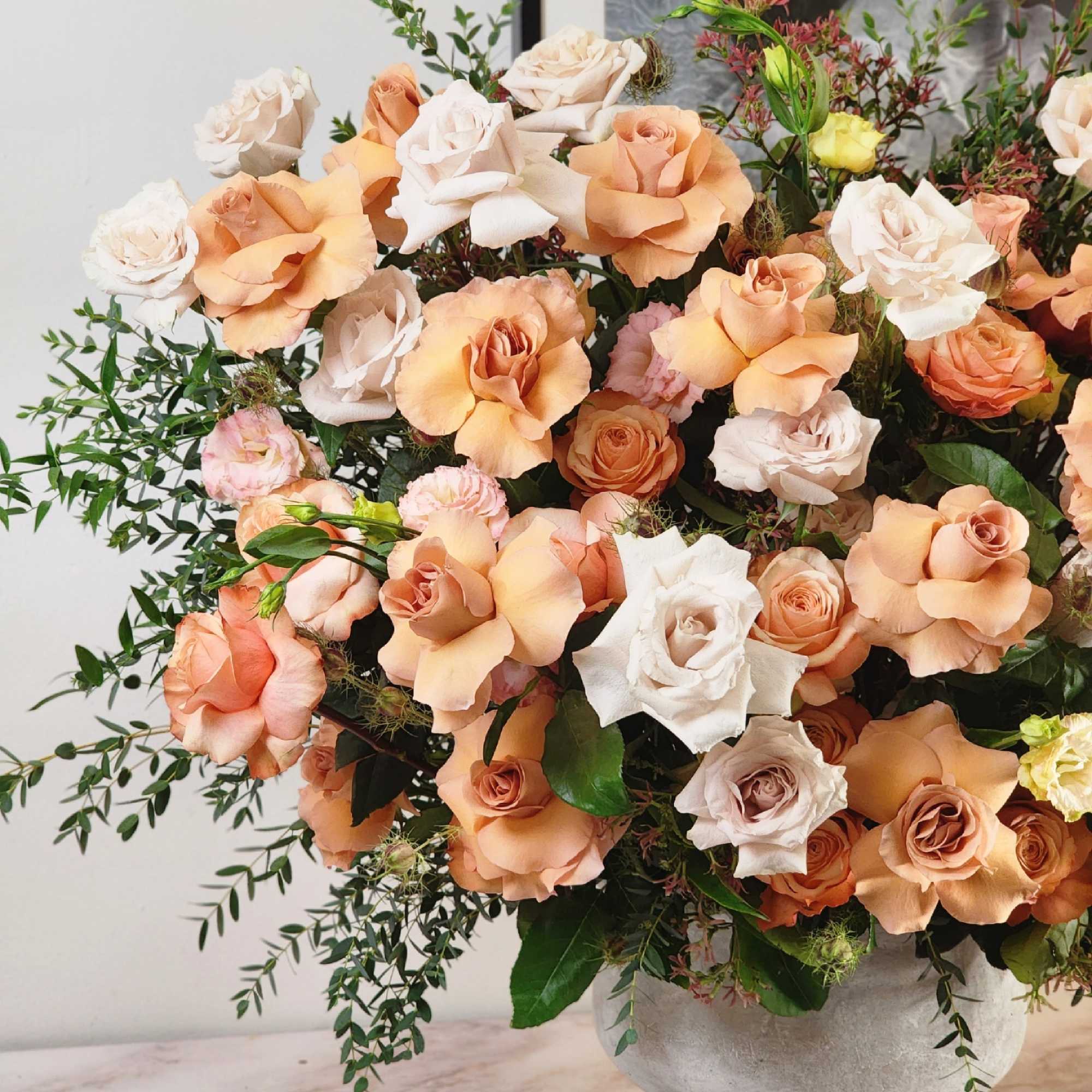 A grandiose vase holds an enchanting blend of beige and peach roses