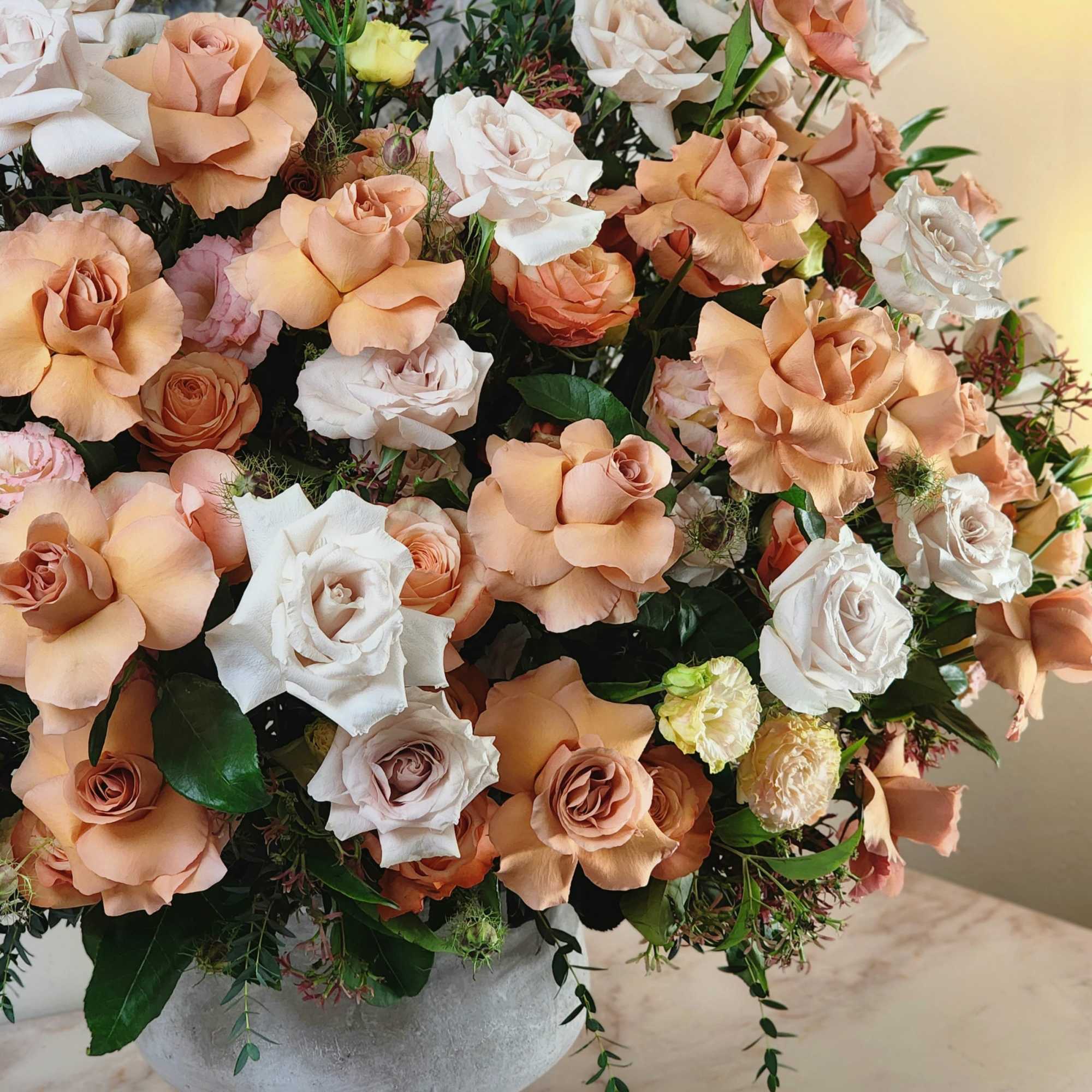 A grandiose vase holds an enchanting blend of beige and peach roses