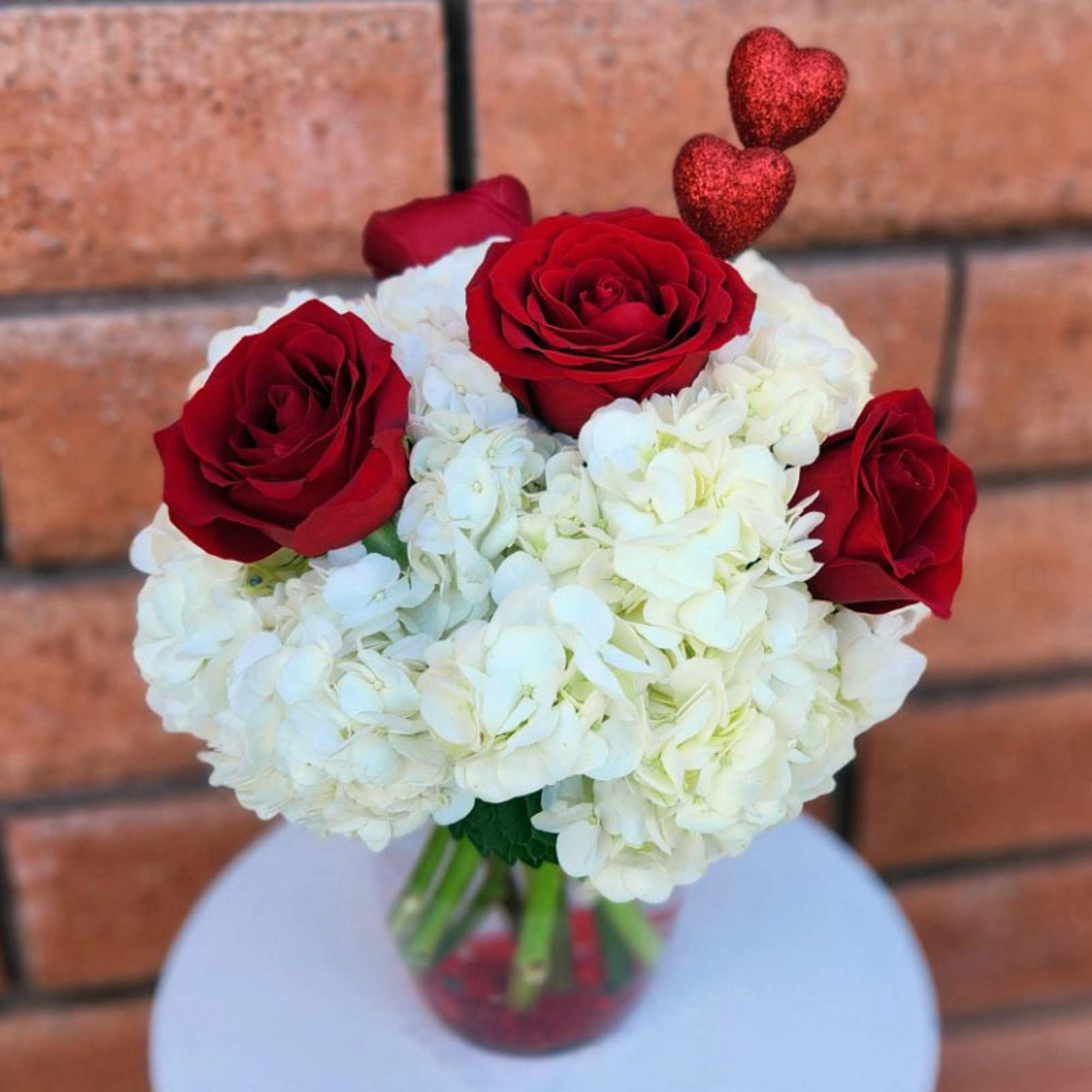 This beautiful arrangement features four premium red roses and three white hydrangeas.