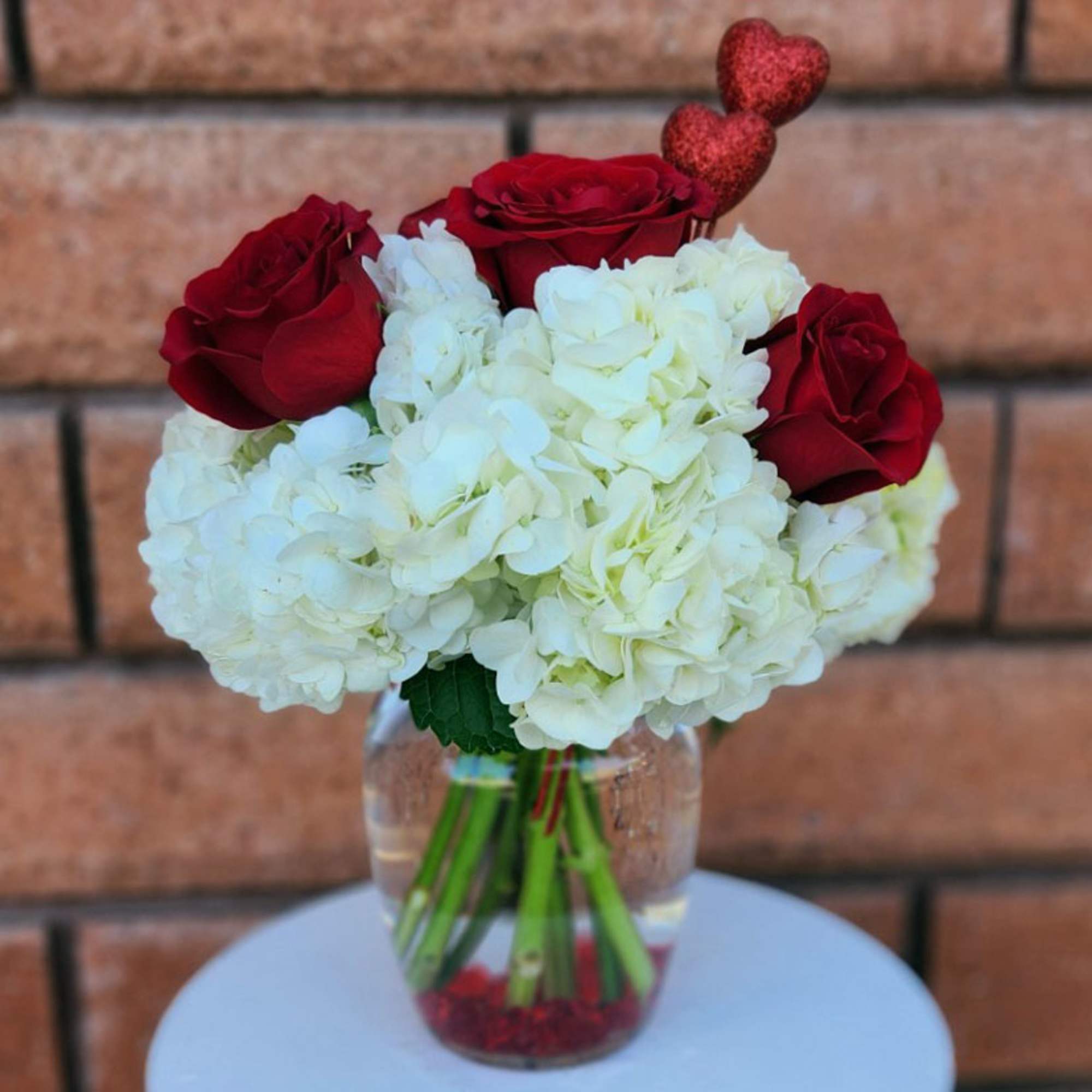 This beautiful arrangement features four premium red roses and three white hydrangeas.