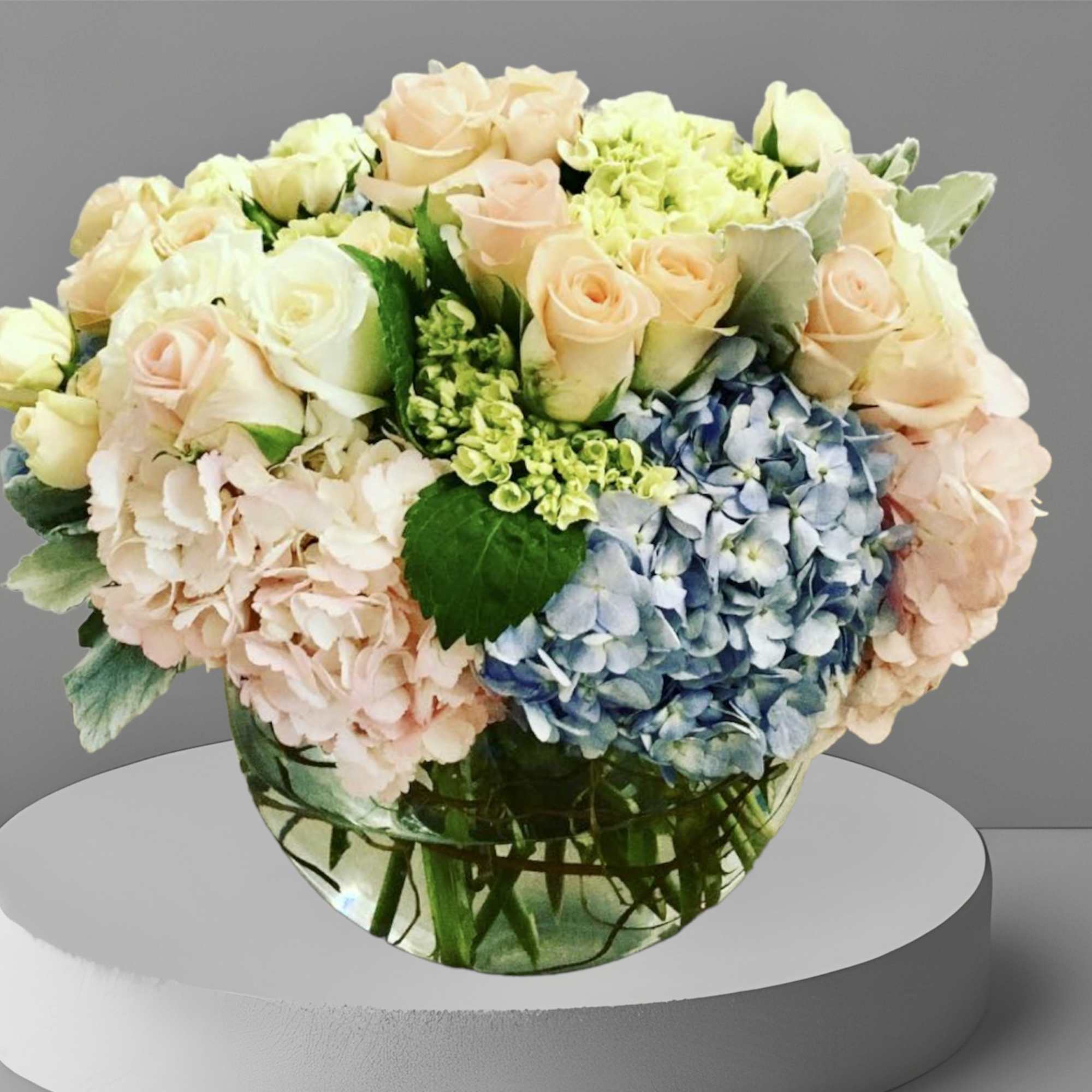 A gorgeous mix of pastel hydrangea and roses with seasonal foliage arranged