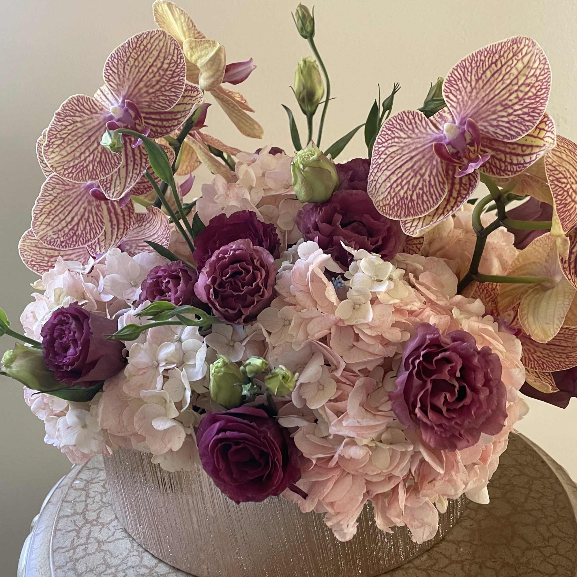 Peach/ pinkish Hydrangeas, Purple lisianthus, orchids in rose gold ceramic vessel.