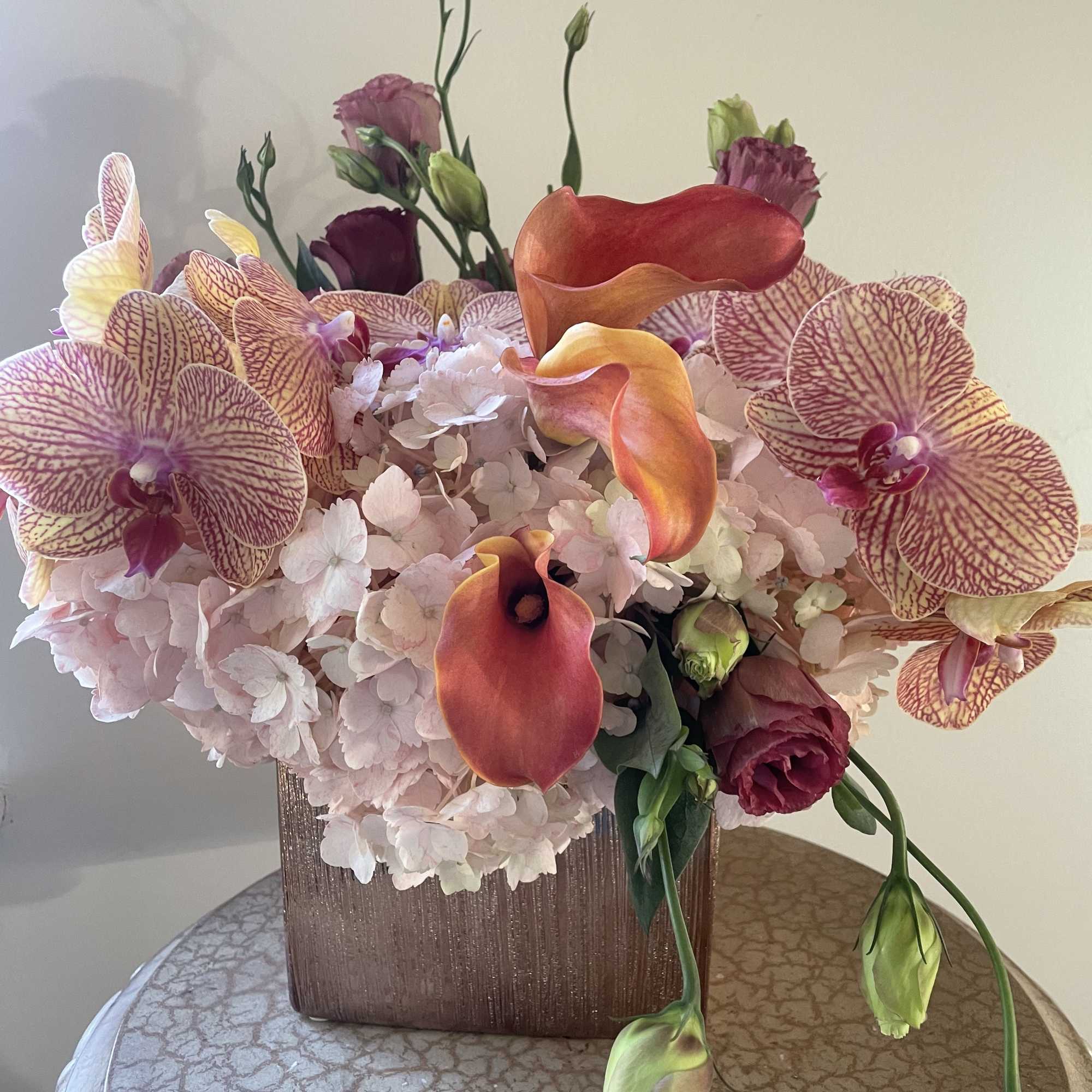 Peach/ pinkish Hydrangeas, Purple lisianthus, orchids in rose gold ceramic vessel.