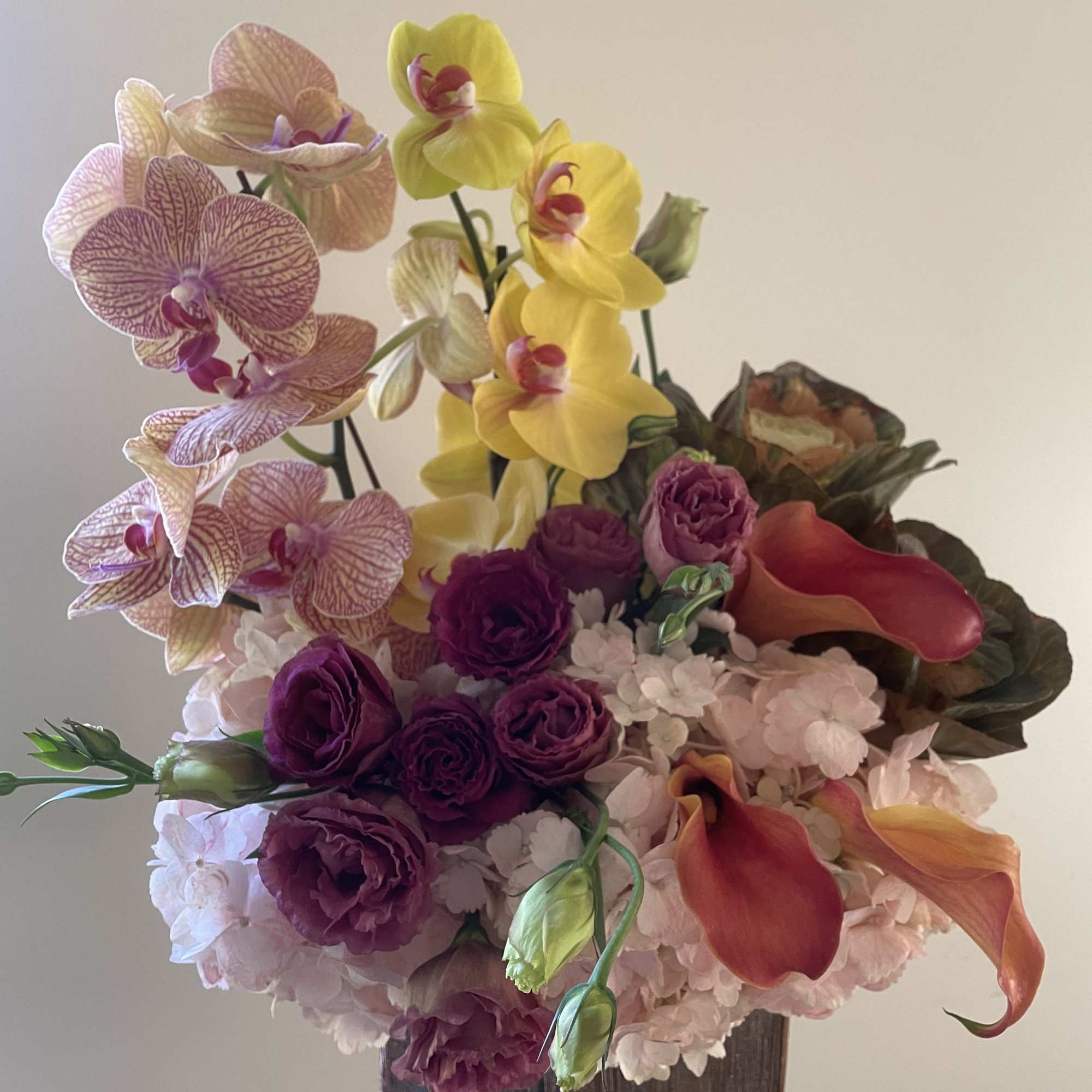 Peach/ pinkish Hydrangeas, Purple lisianthus, orchids in rose gold ceramic vessel.