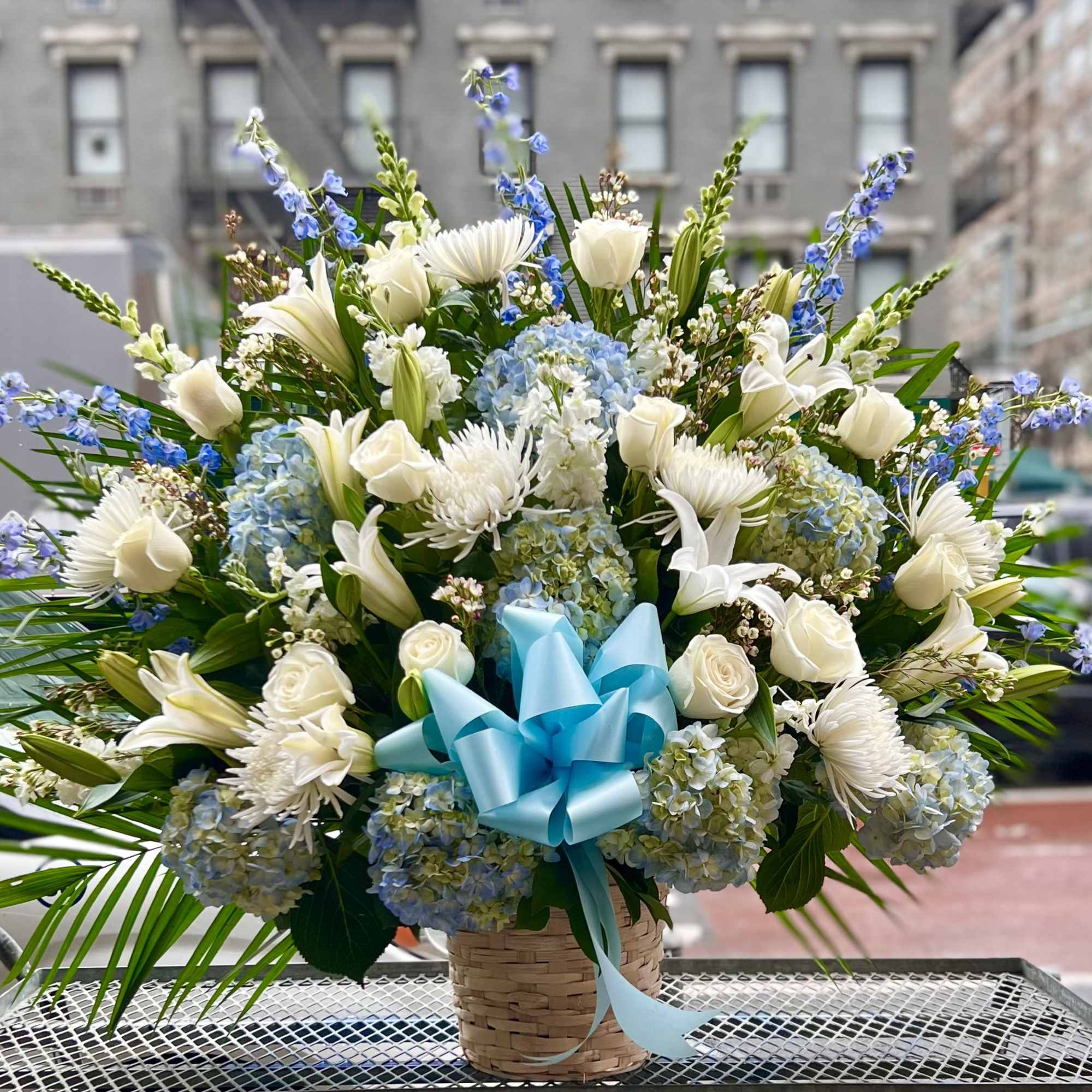 This beautiful white and blue flower basket includes Hydrangeas, Roses, Delphinium and