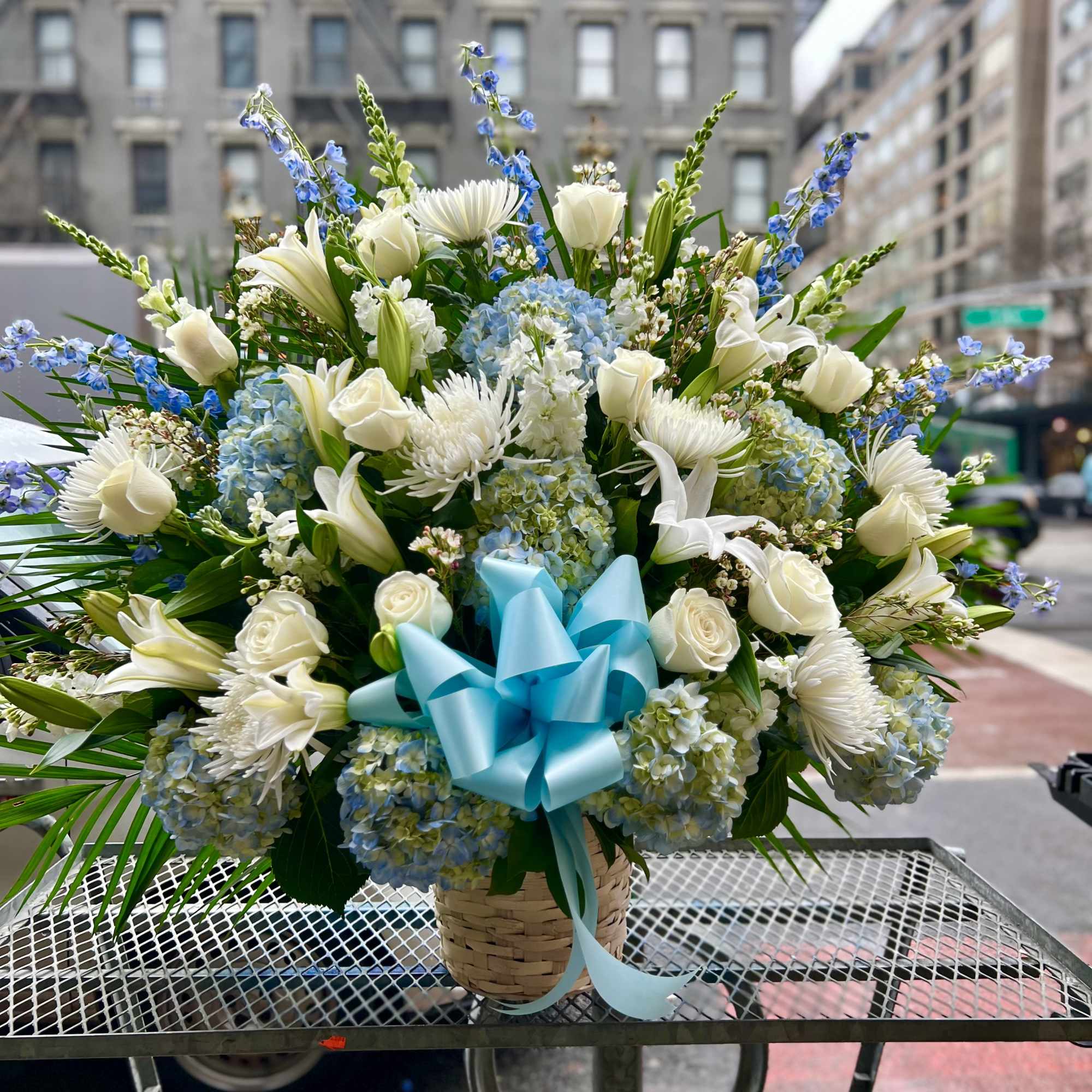 This beautiful white and blue flower basket includes Hydrangeas, Roses, Delphinium and
