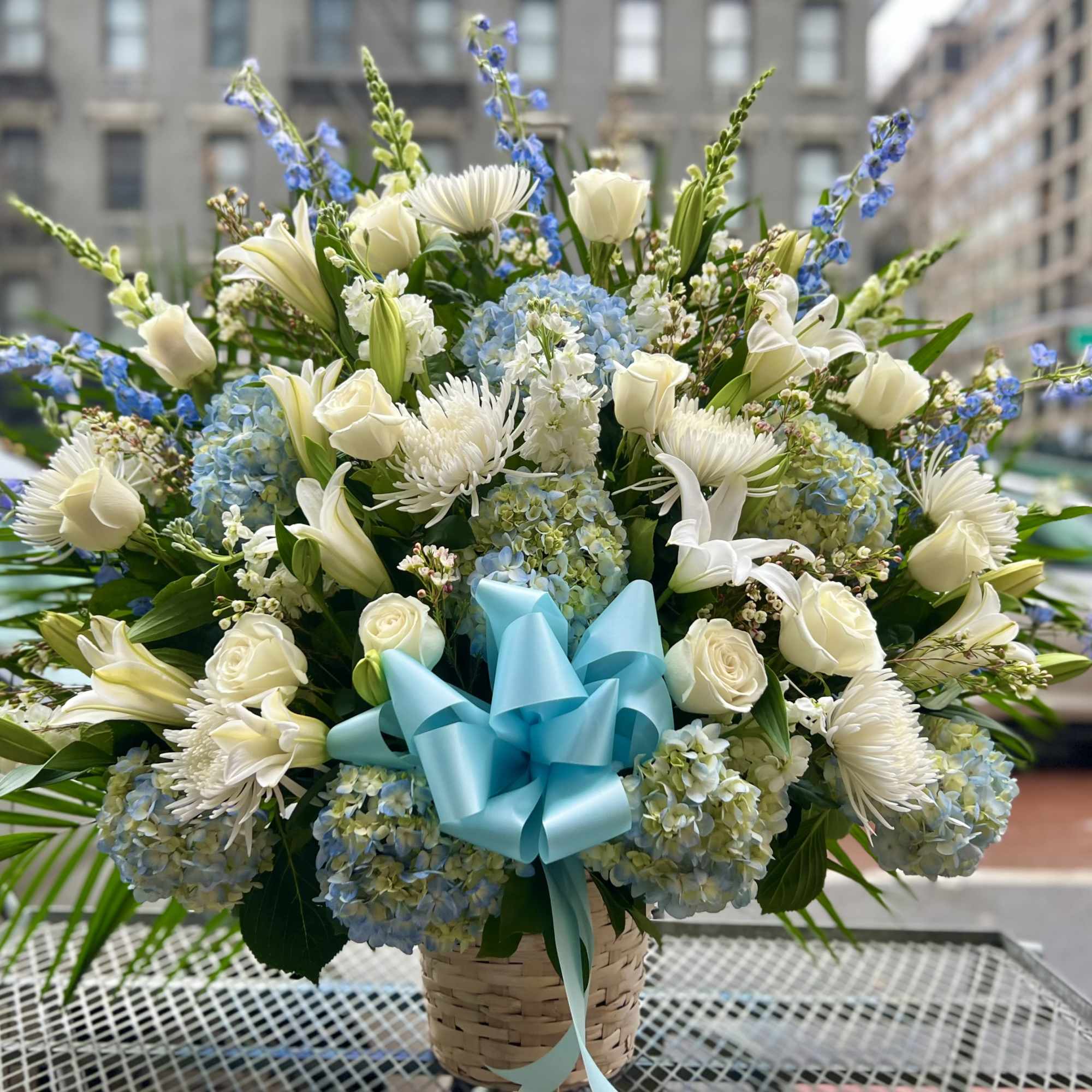 This beautiful white and blue flower basket includes Hydrangeas, Roses, Delphinium and