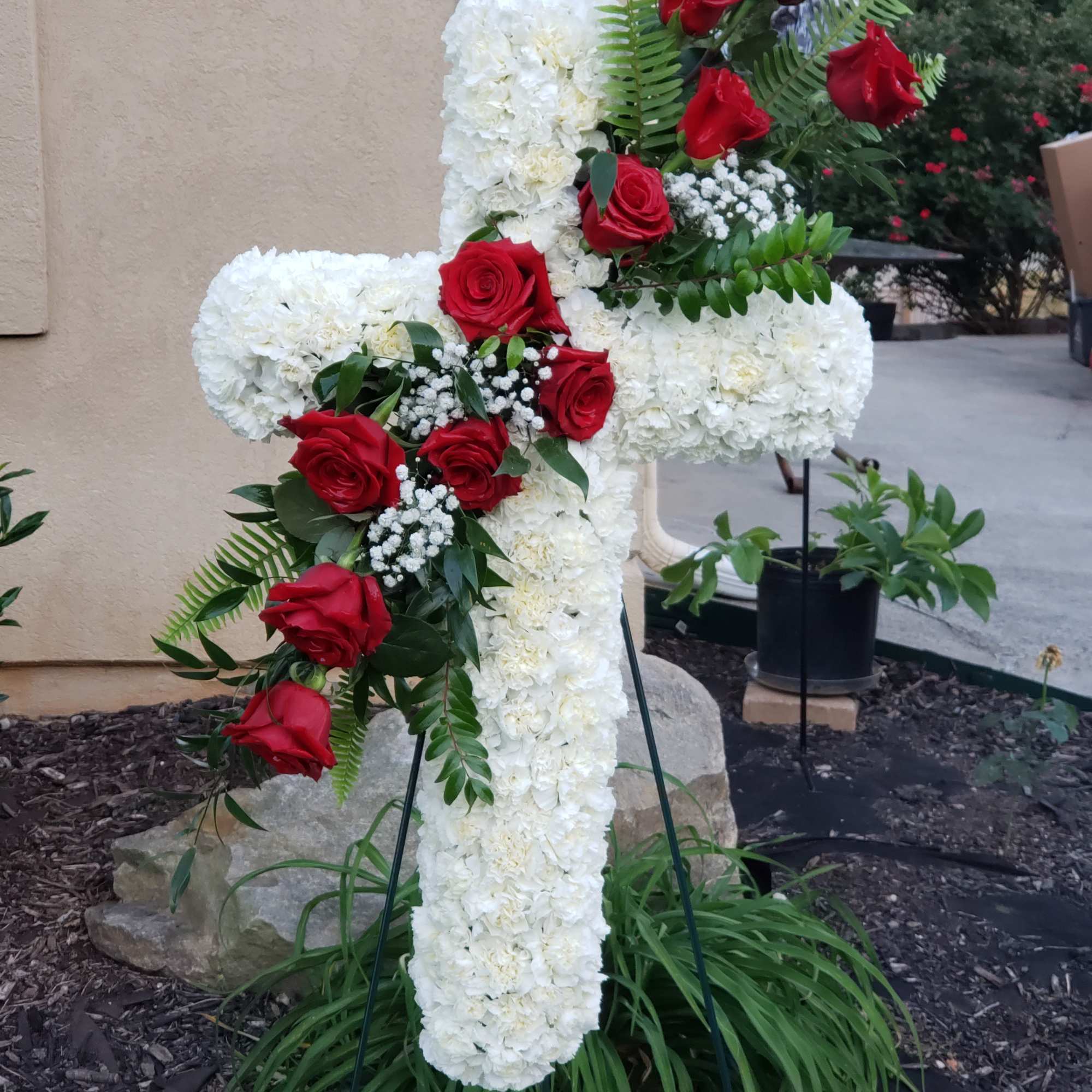 Standing spray cross of white blossoms (carnations) adorned with red roses. It’s Standing spray cross of white blossoms (carnations) adorned with red roses. It’s