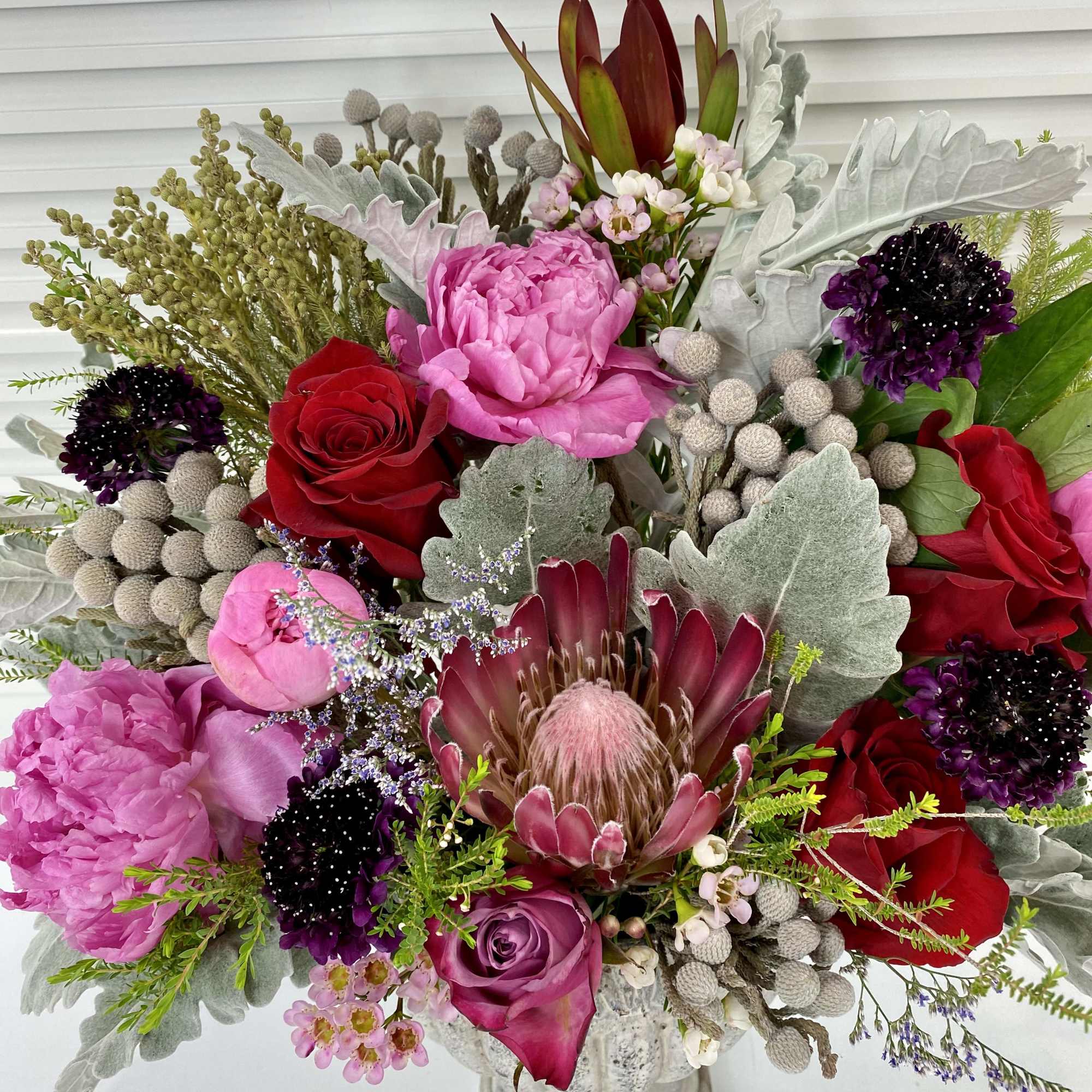 Elegant flower arrangement with peonies, roses, protea and wax flower surrounded by