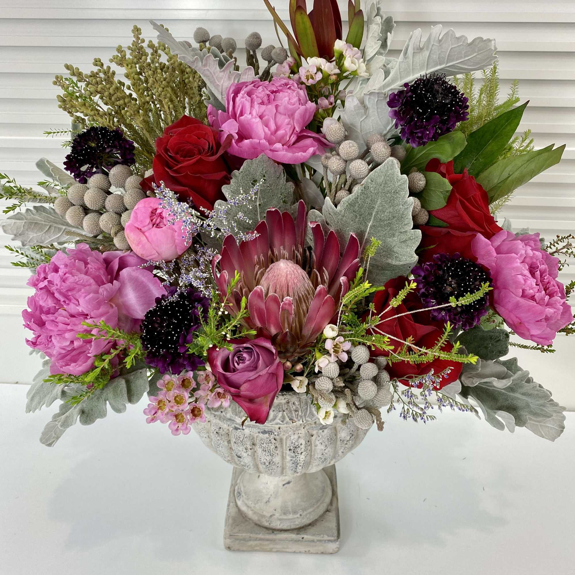 Elegant flower arrangement with peonies, roses, protea and wax flower surrounded by