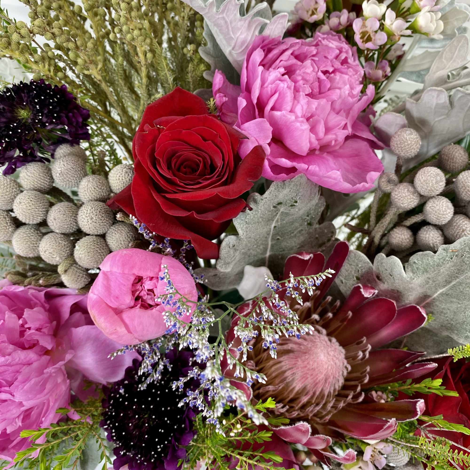 Elegant flower arrangement with peonies, roses, protea and wax flower surrounded by