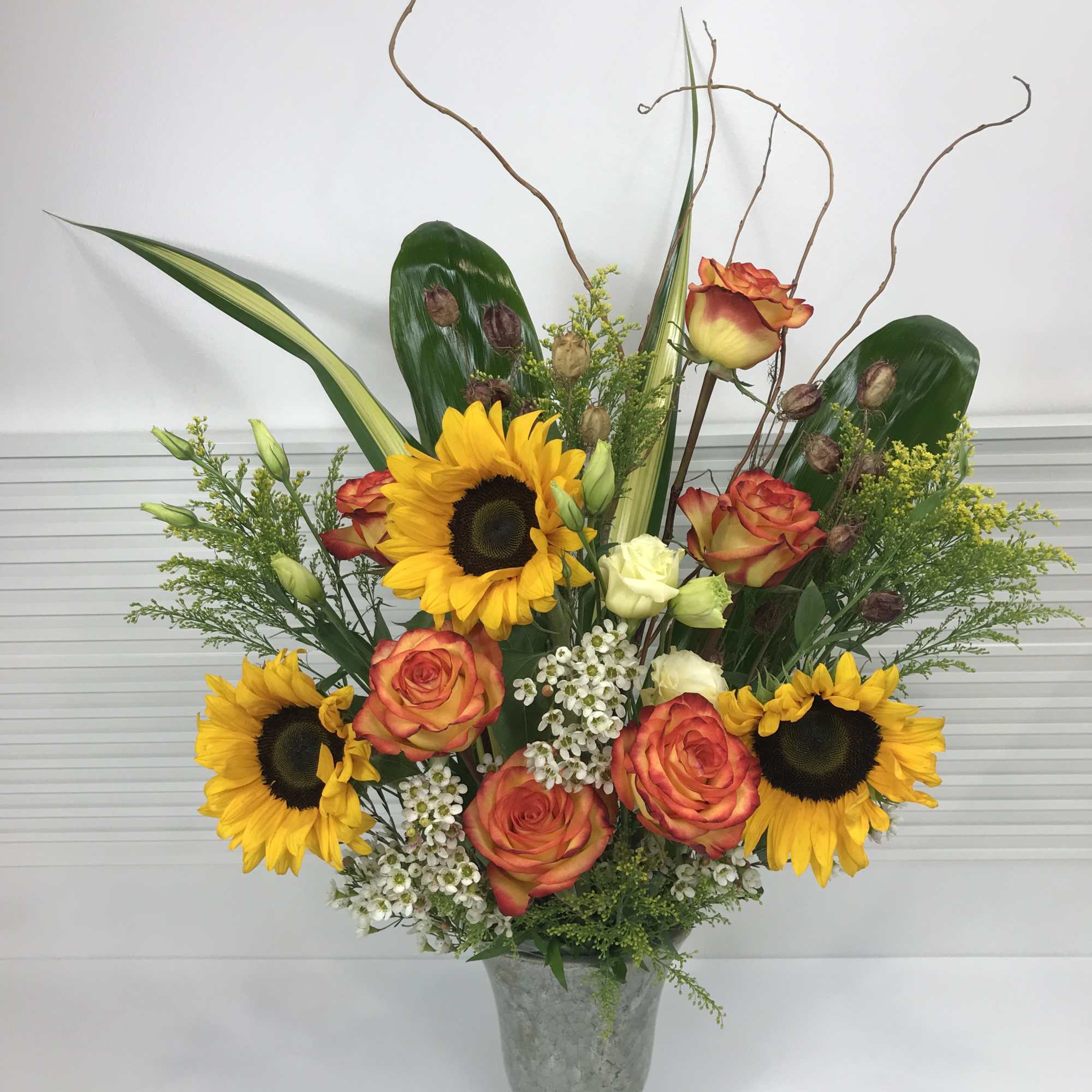 Antique pottery vase filled with large Sunflowers, Roses, Lisianthus, and variety of