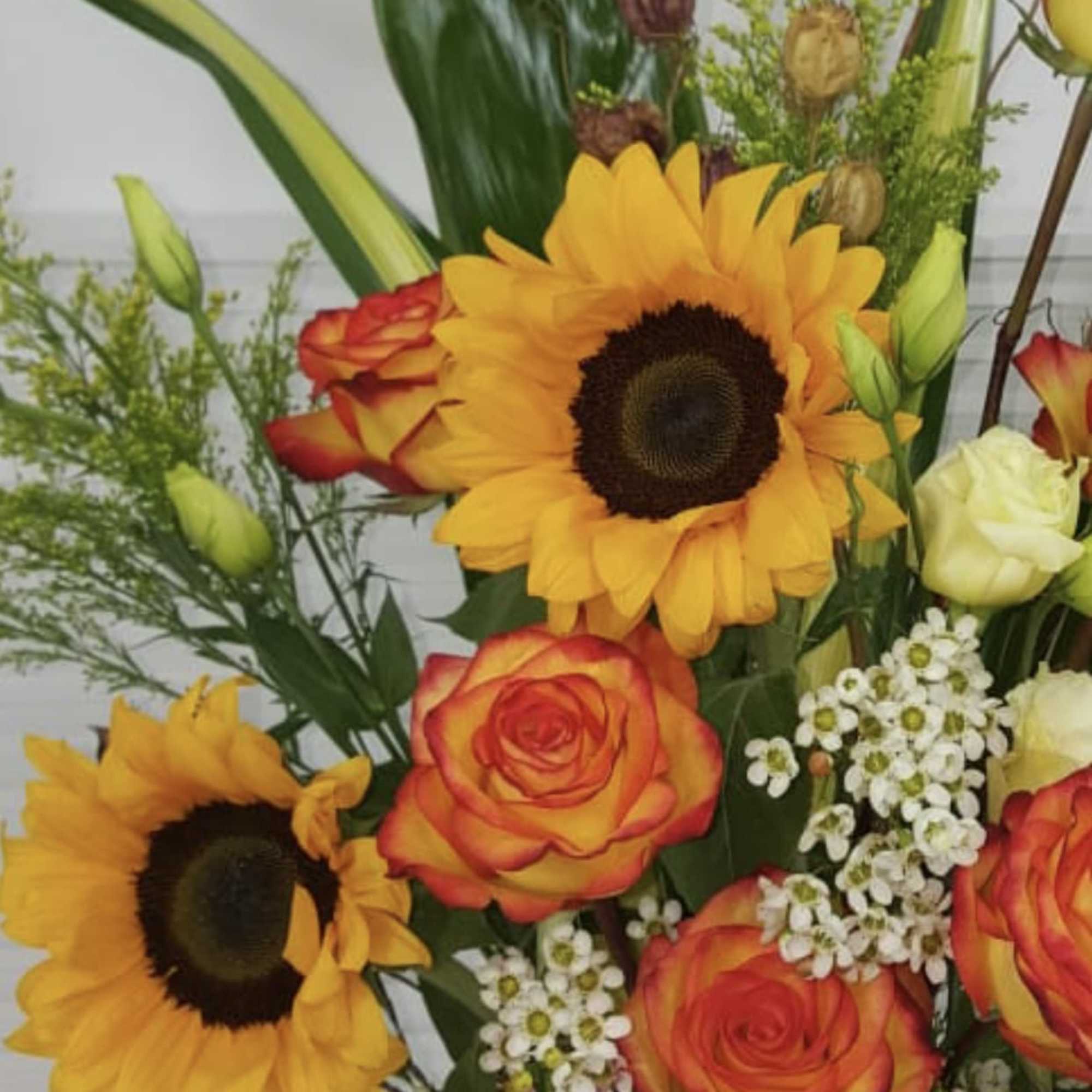 Antique pottery vase filled with large Sunflowers, Roses, Lisianthus, and variety of