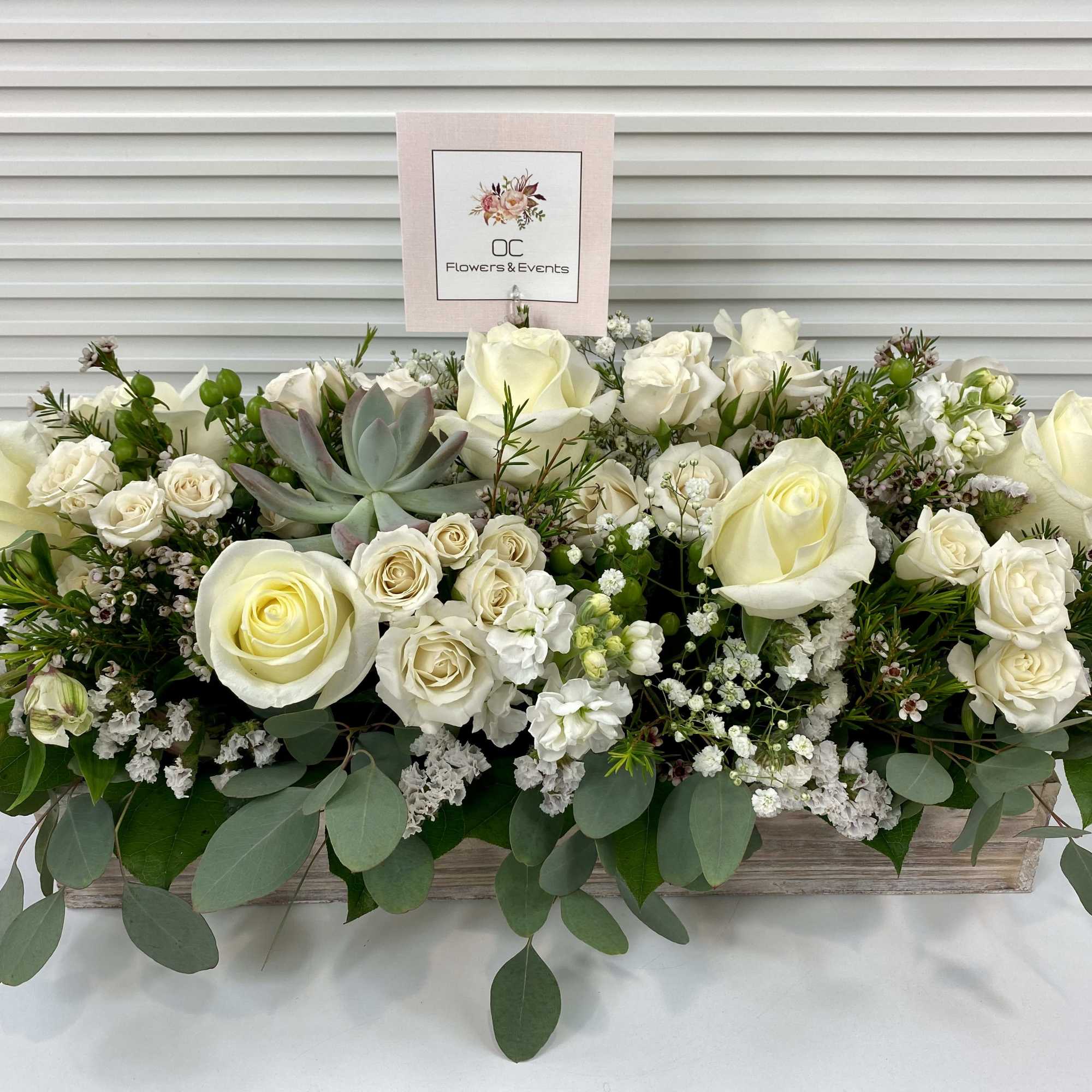 Elegant white and green sympathy flower arrangement in a long wooden tray.