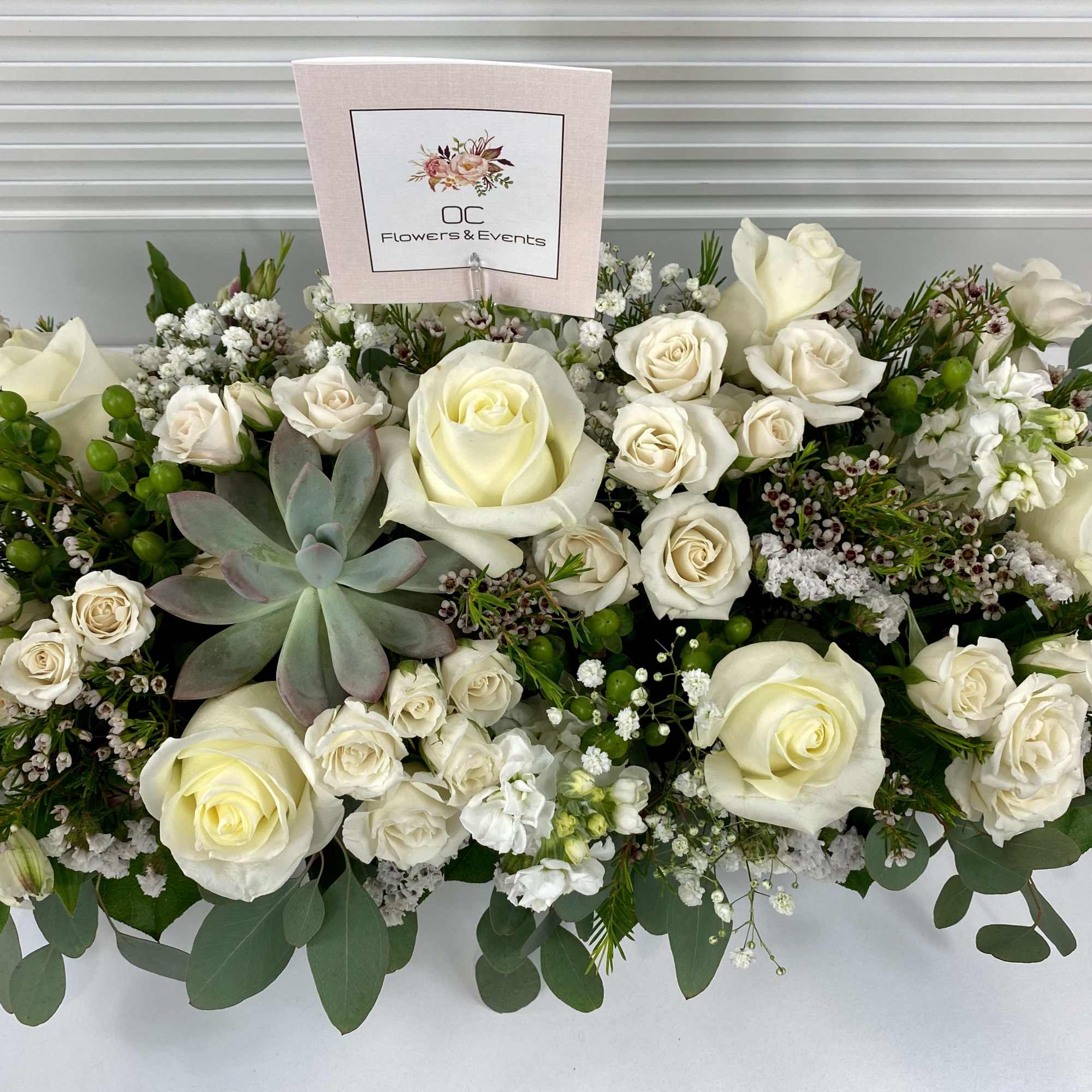 Elegant white and green sympathy flower arrangement in a long wooden tray.