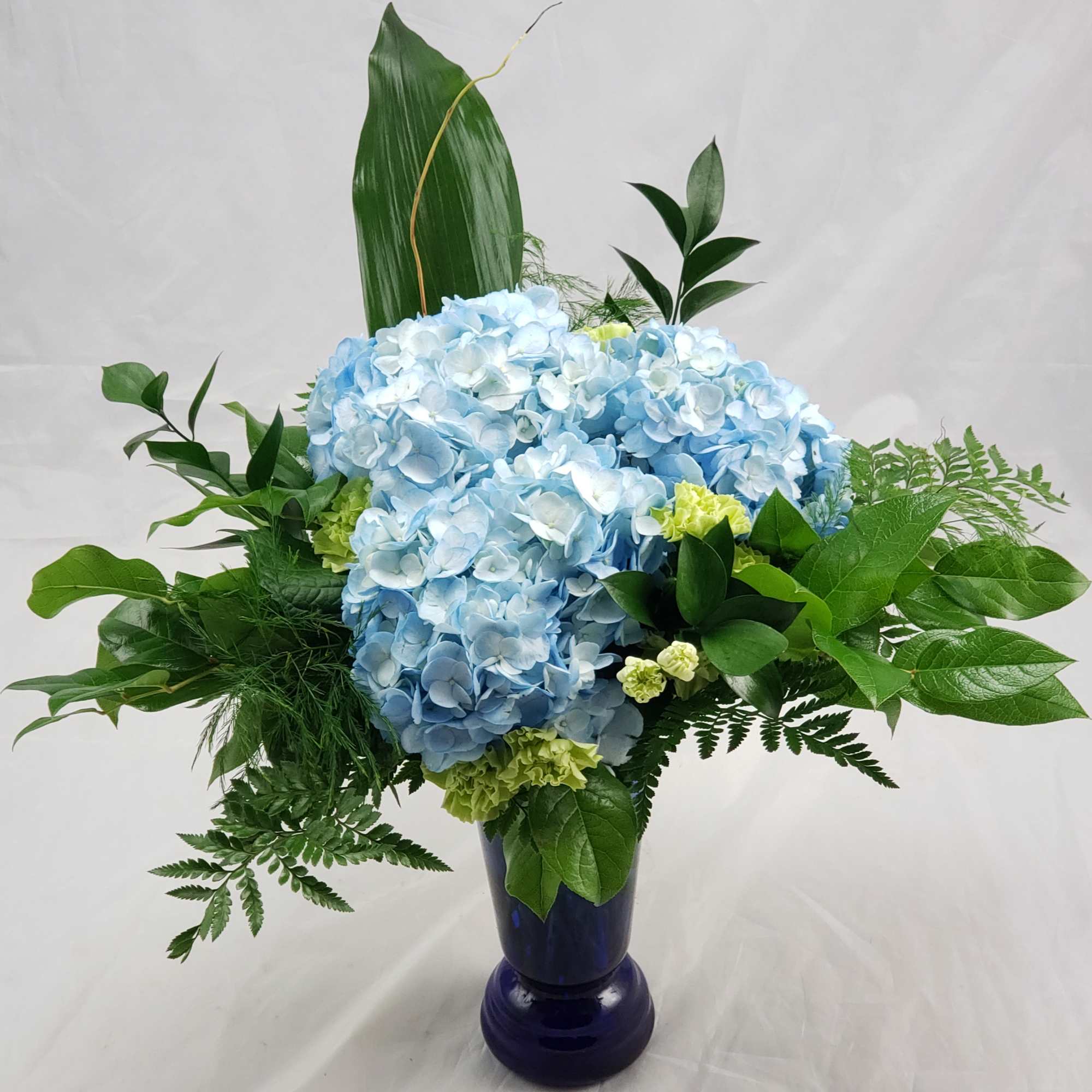 A beautifully arranged vase filled with Blue Hydrangeas and mixed greens (vase