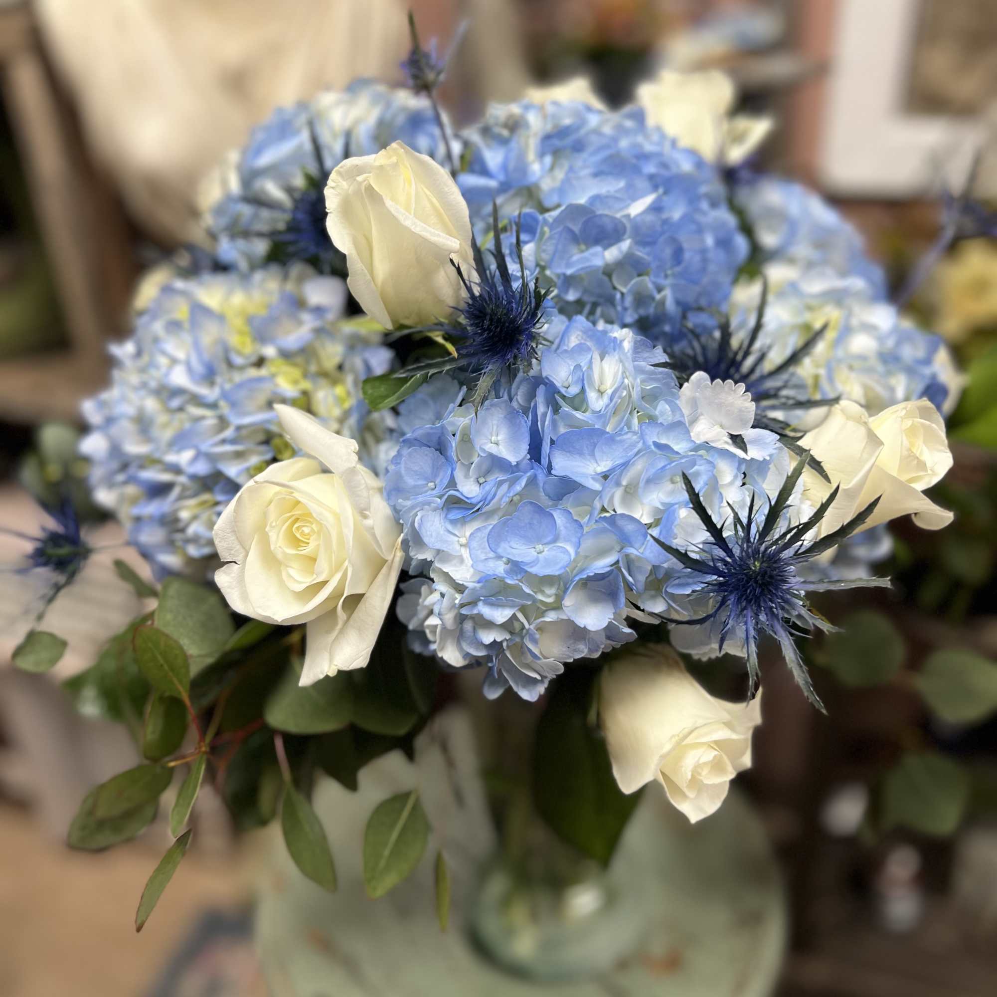 A beautifully arranged vase filled with Blue Hydrangeas and mixed greens (vase