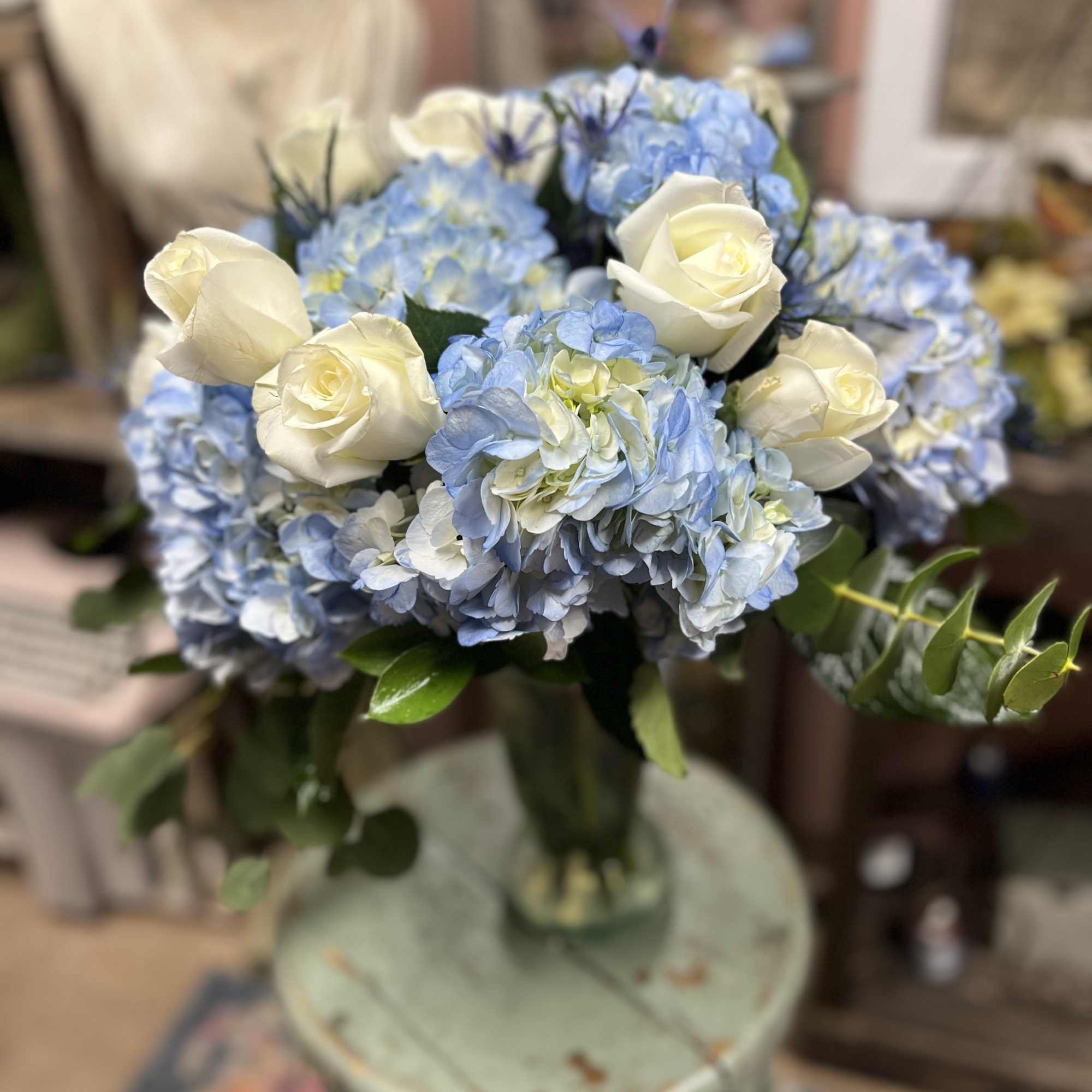 A beautifully arranged vase filled with Blue Hydrangeas and mixed greens (vase