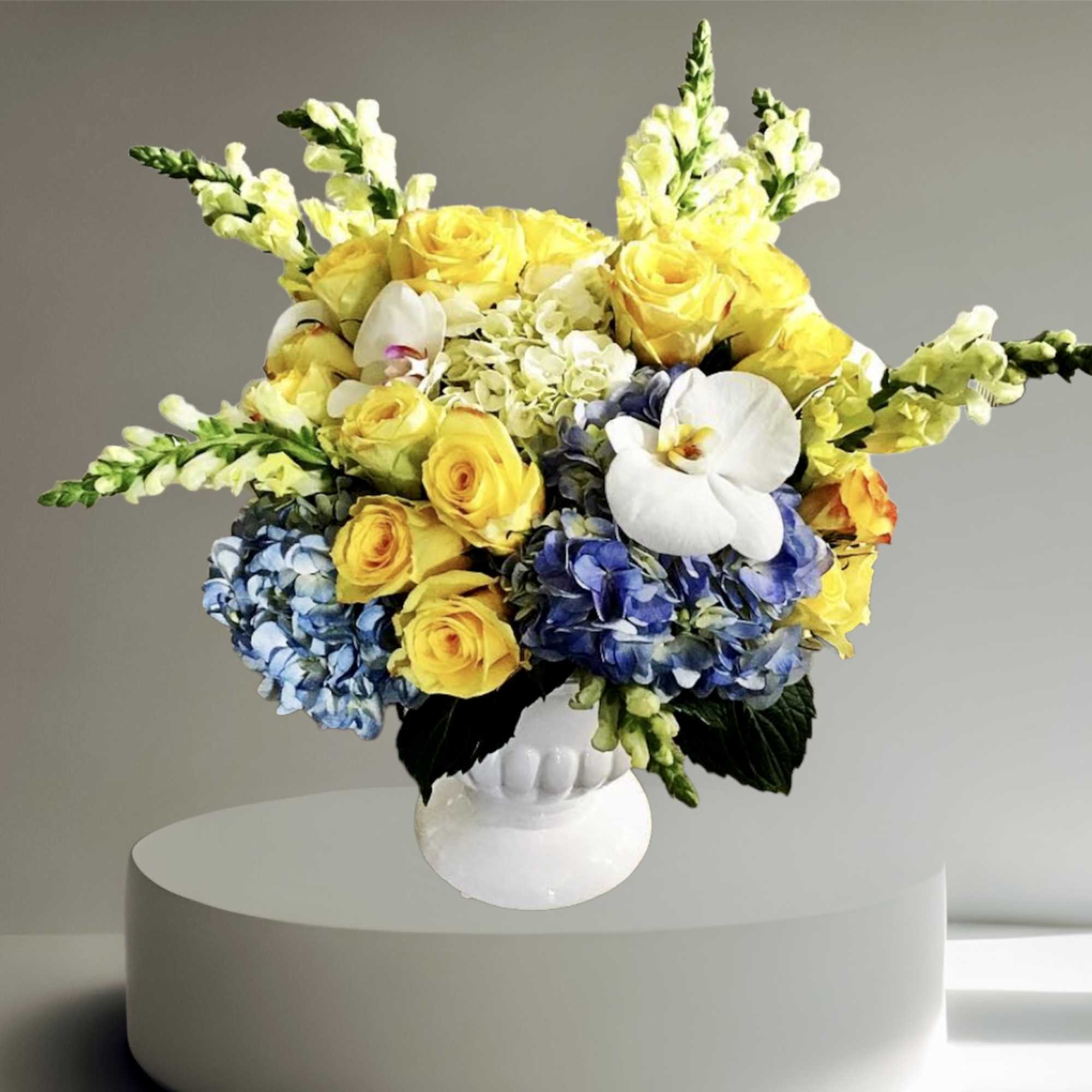 A grand arrangement with blue hydrangea, yellow roses, orchids, and snapdragon arranged