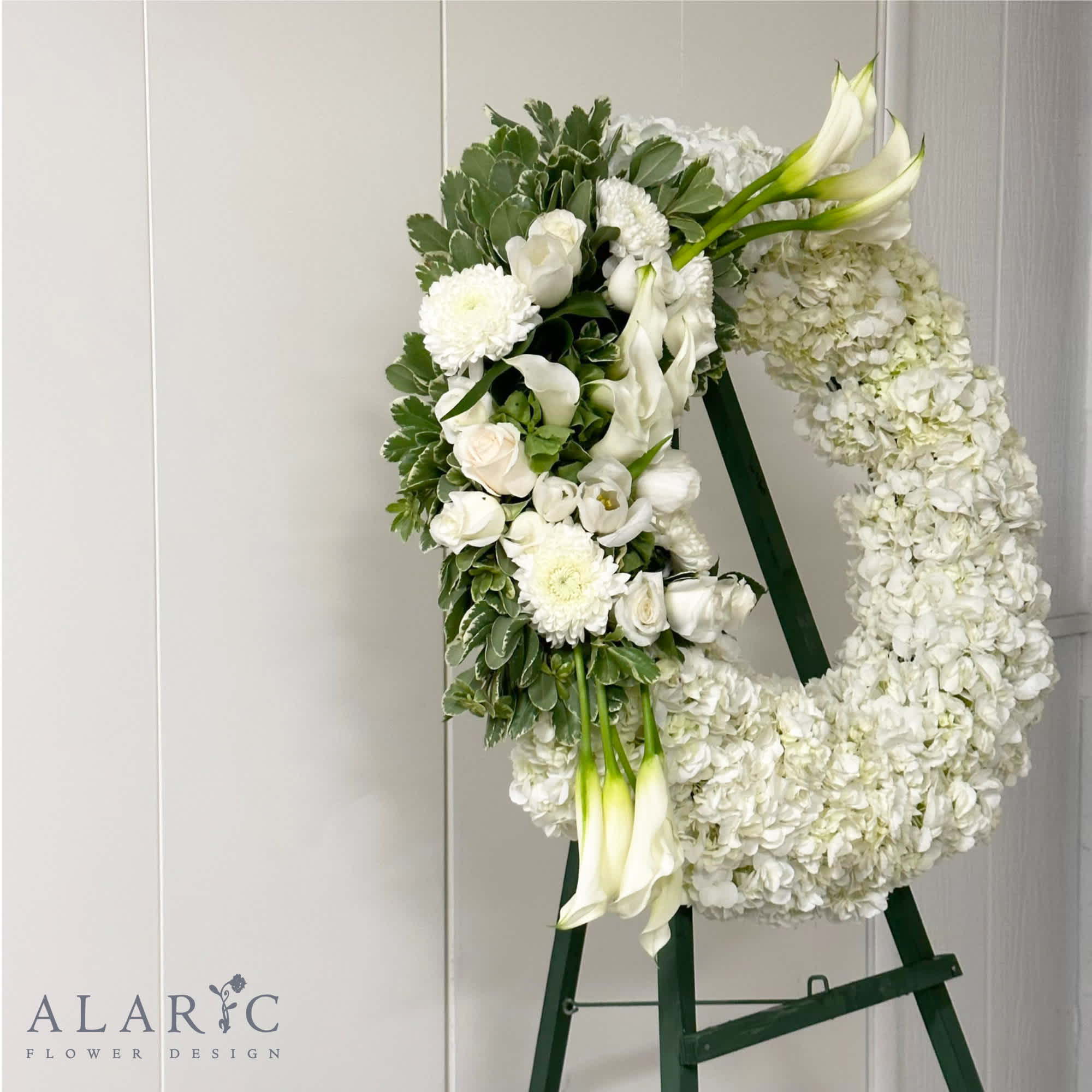 An all white, large funeral wreath on a stand to show love