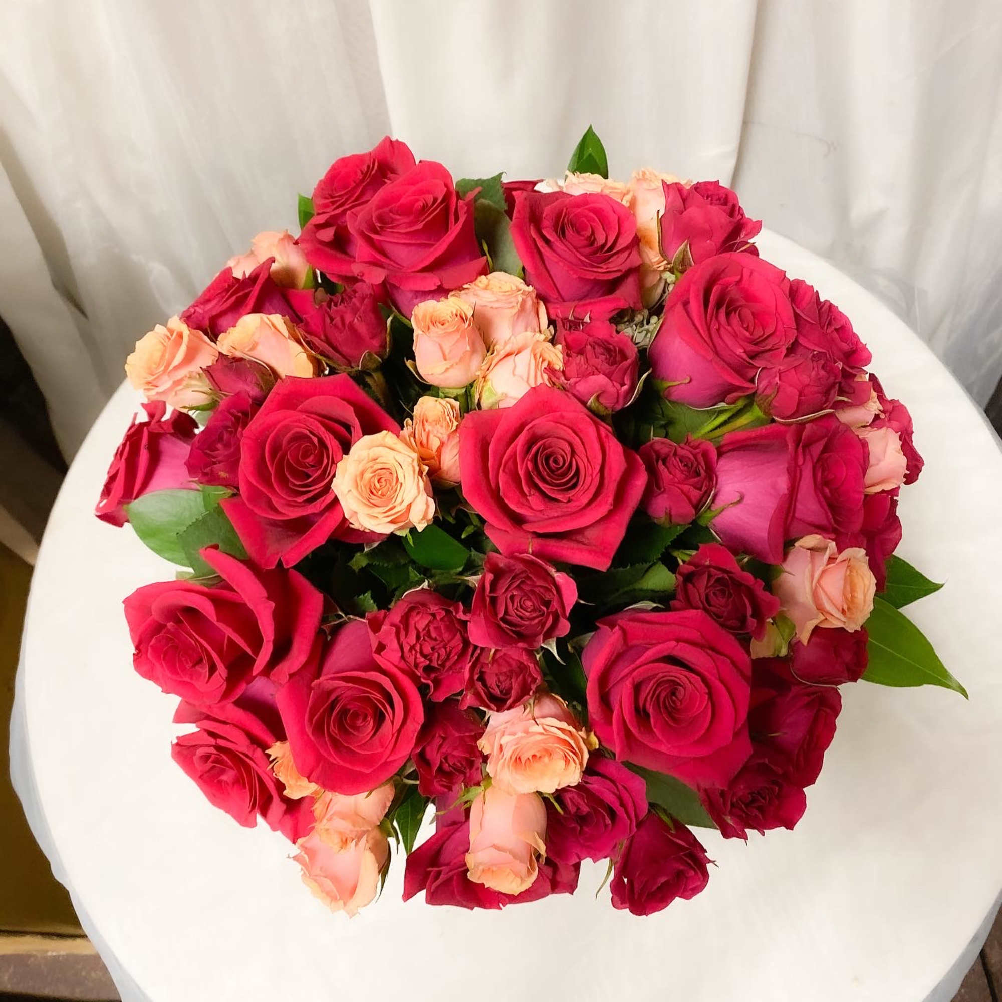 Bright arrangement of roses and spray roses in a glass cube. Simple