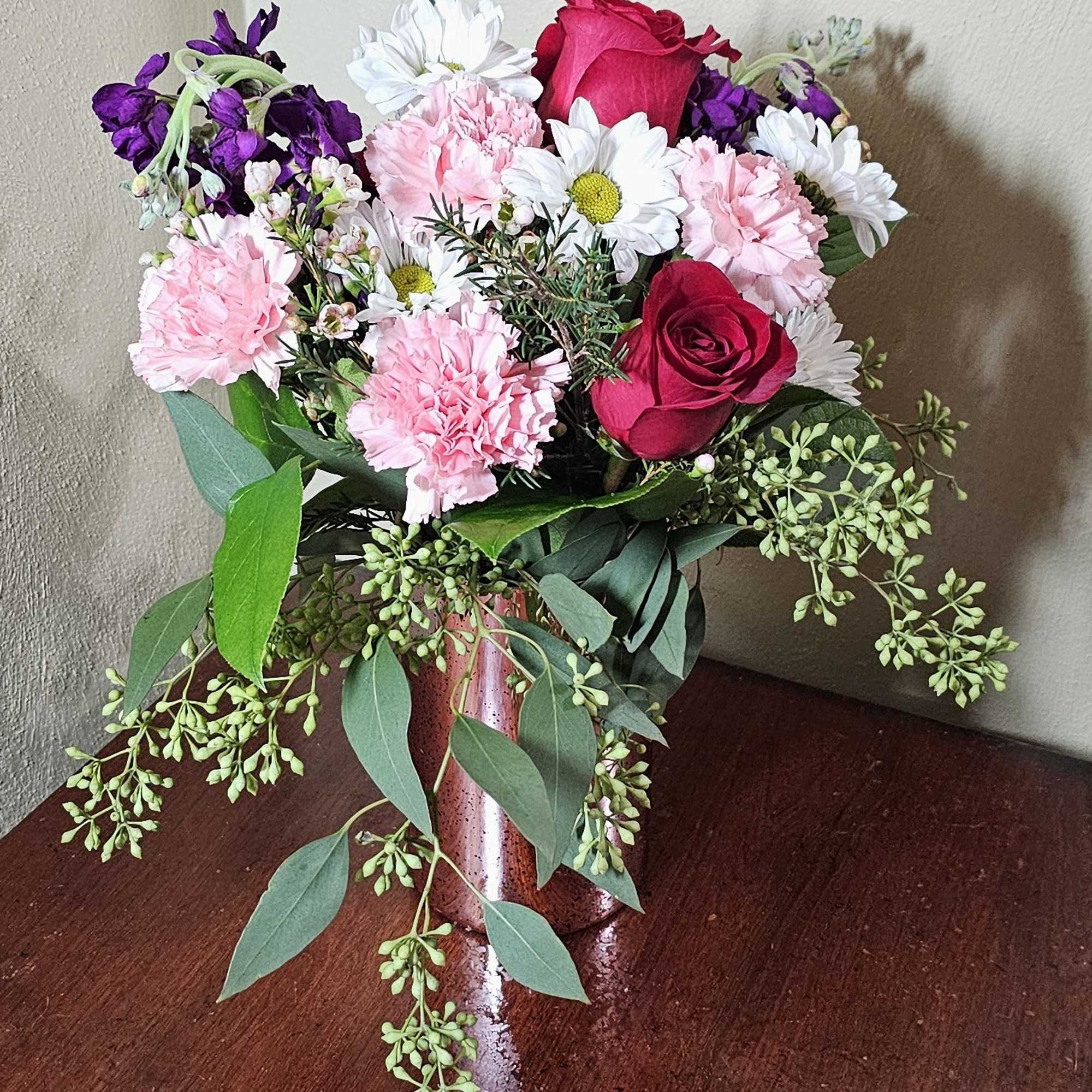 Pink reflective vase with assortment of pink, white, and purple flowers.