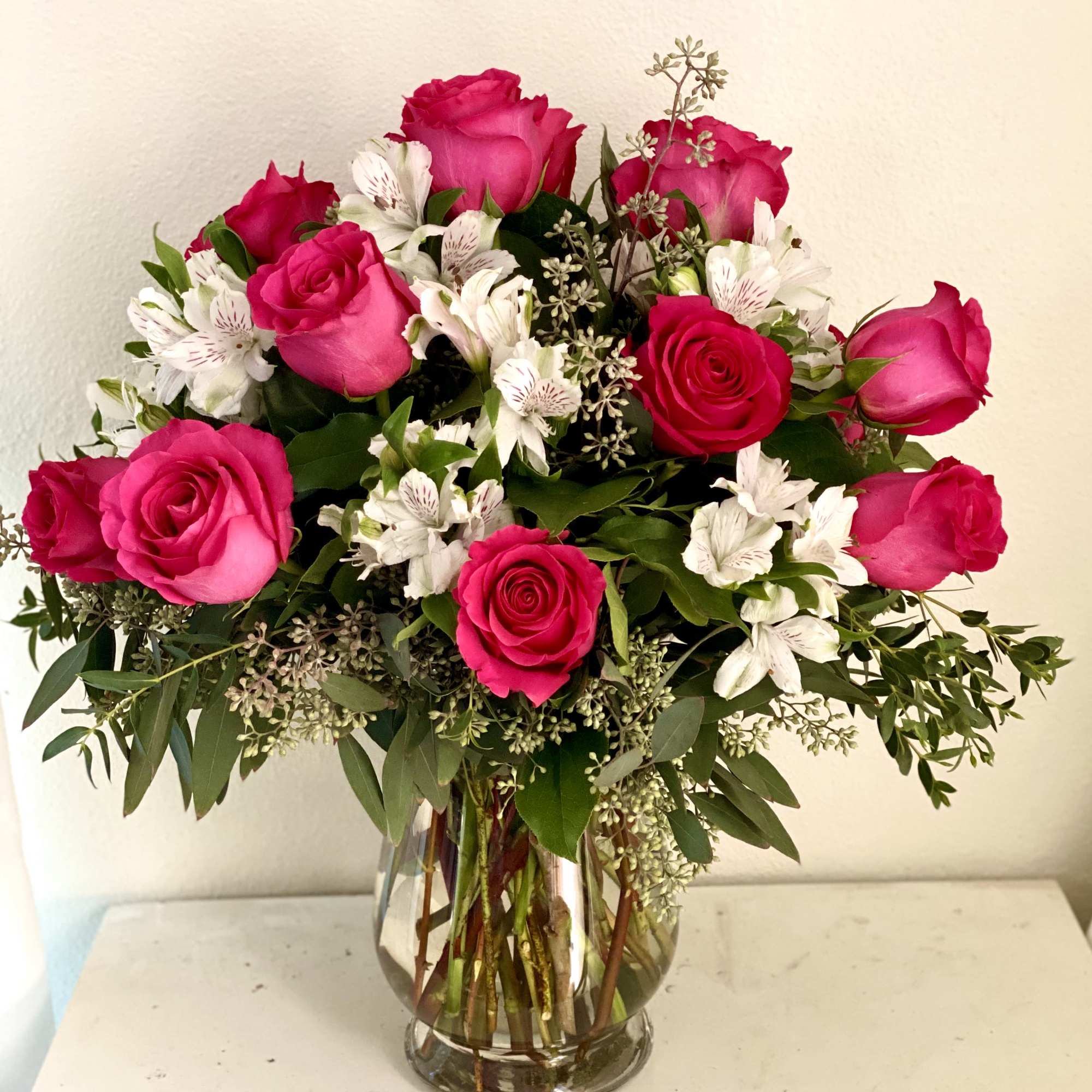A dozen roses arranged with greenery and seasonal fill flowers in a