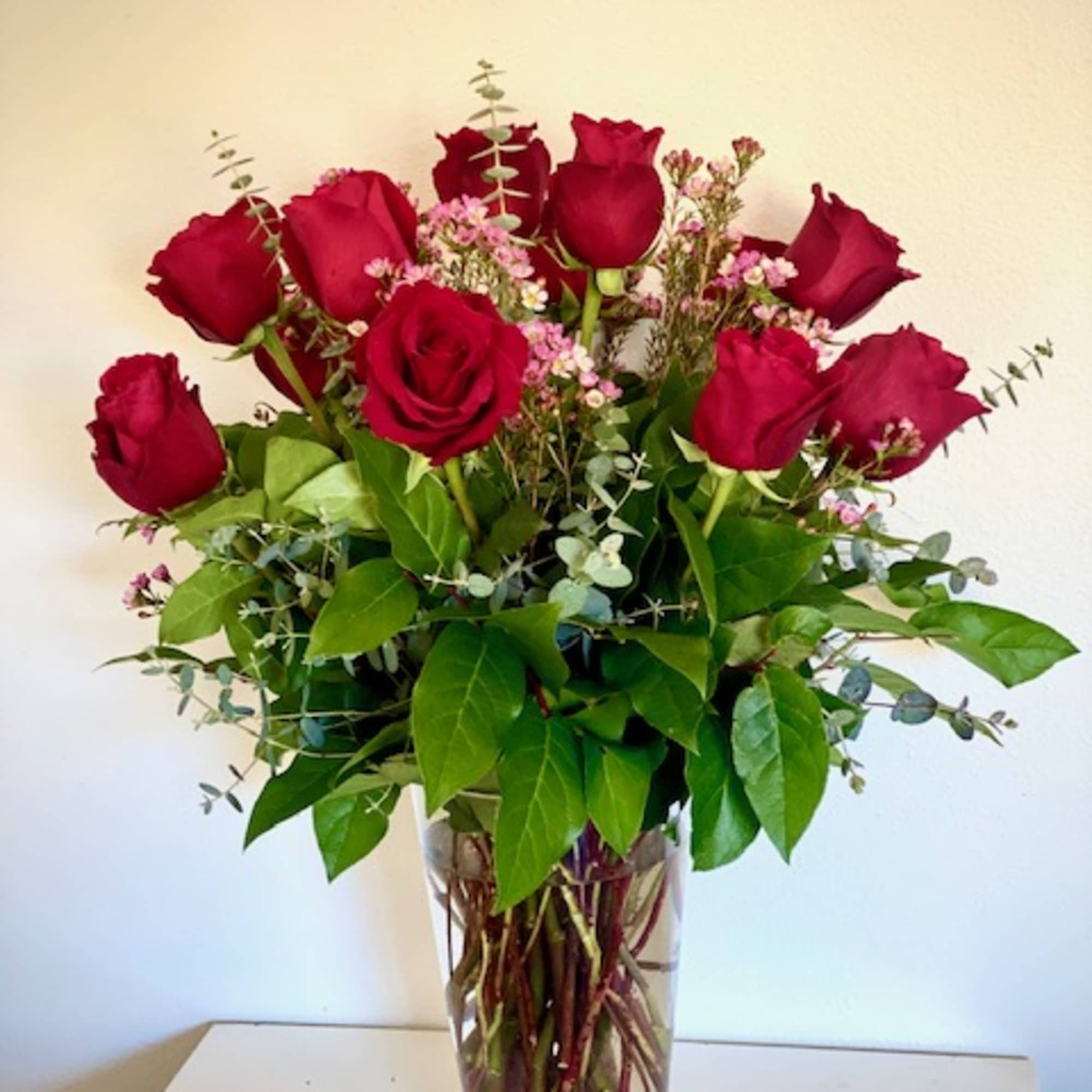 A dozen roses arranged with greenery and seasonal fill flowers in a