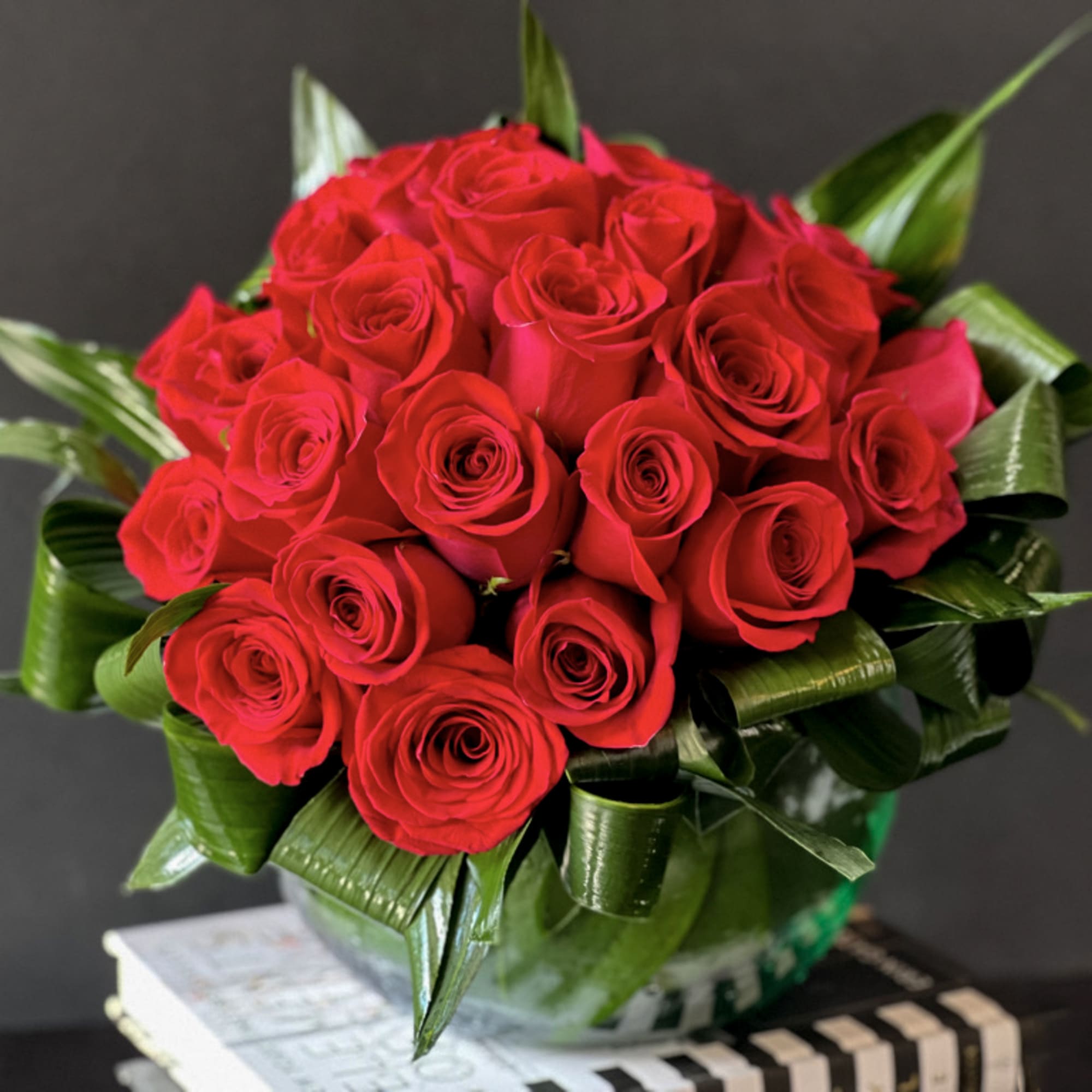 Modern design with 2 dozen red roses in clear vase with greenery