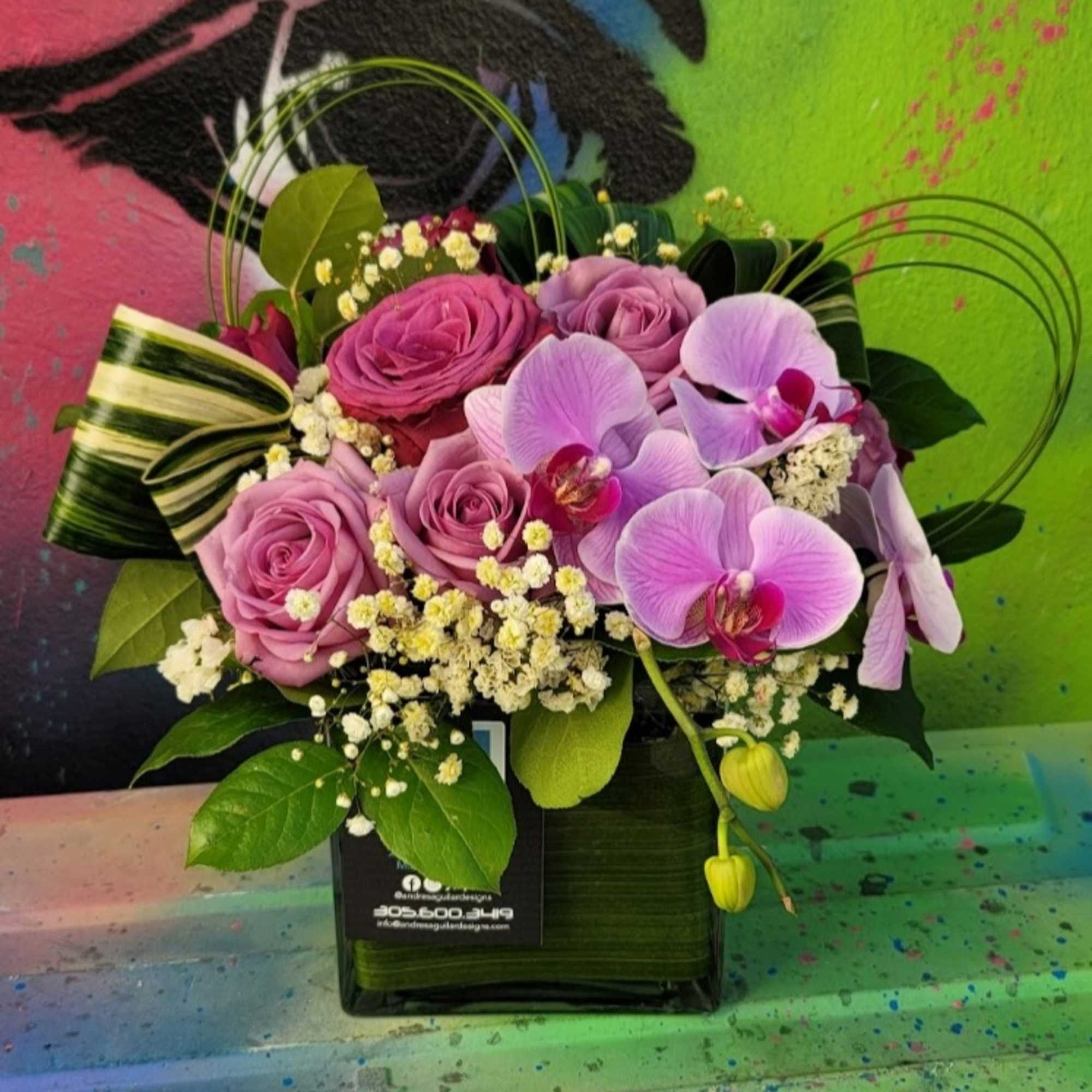 An arrangement in a clear vase with roses, orchids, fillers, and greenery An arrangement in a clear vase with roses, orchids, fillers, and greenery