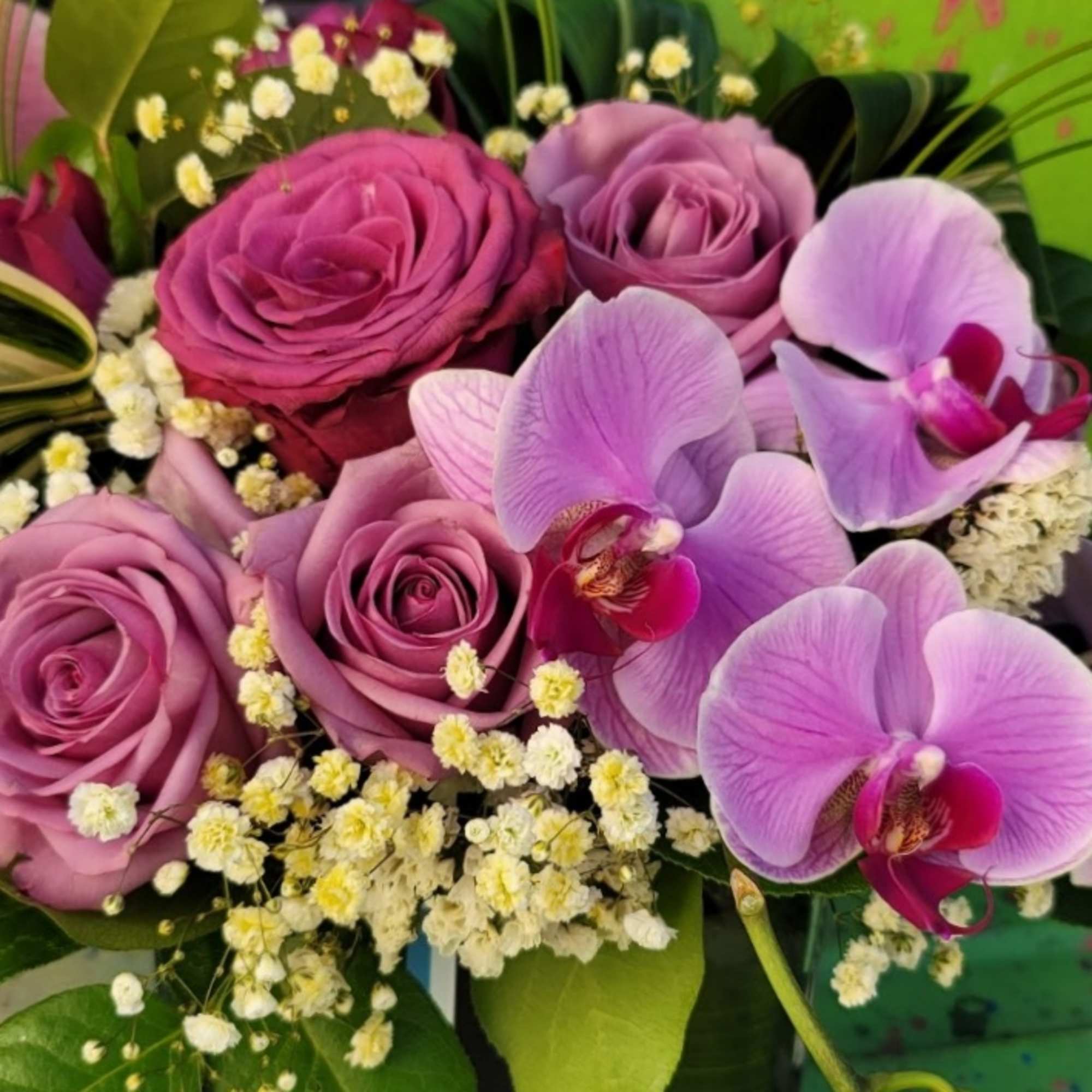 An arrangement in a clear vase with roses, orchids, fillers, and greenery An arrangement in a clear vase with roses, orchids, fillers, and greenery