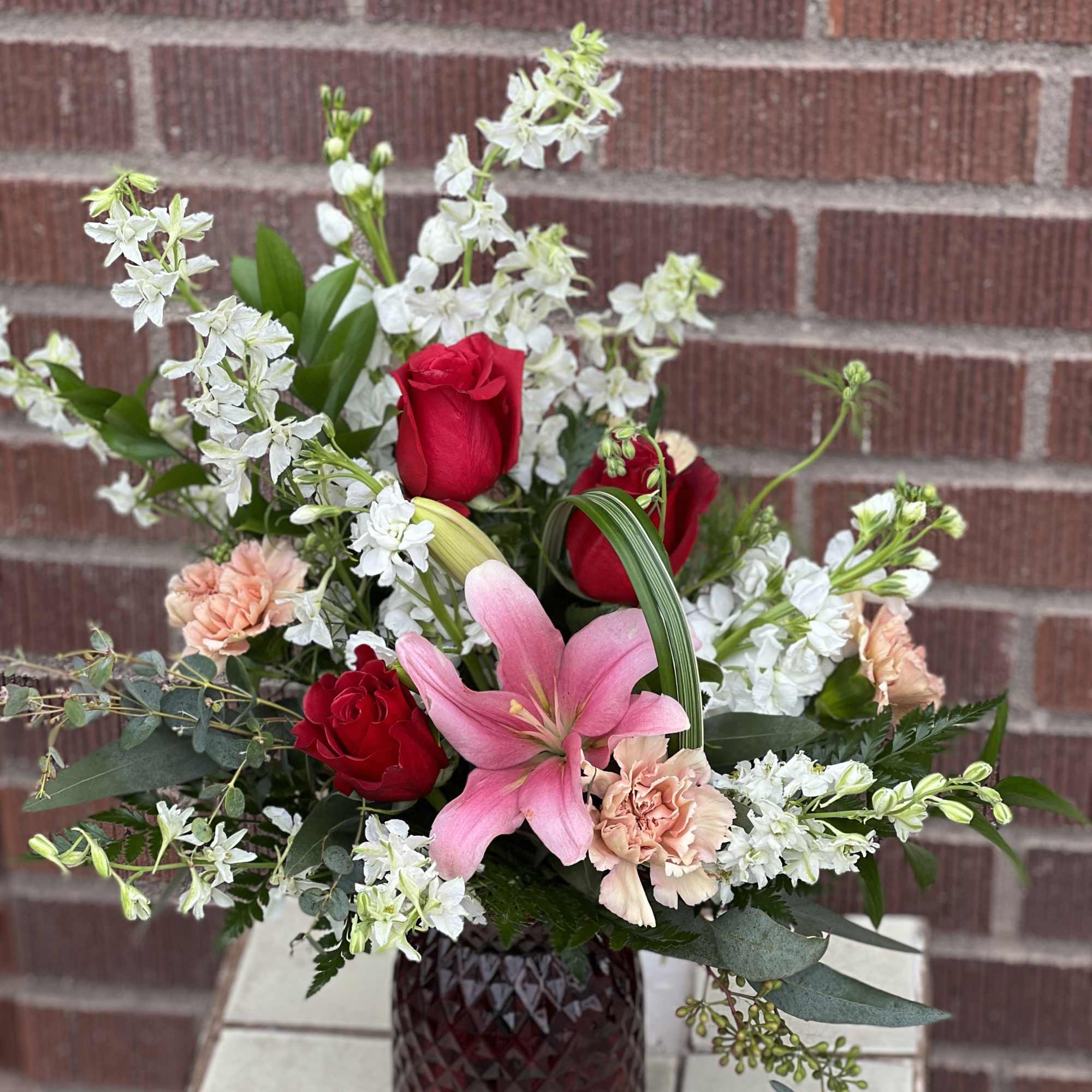 Arriving in diamond cut, embossed vase, this pieces features red roses, lilies Arriving in diamond cut, embossed vase, this pieces features red roses, lilies