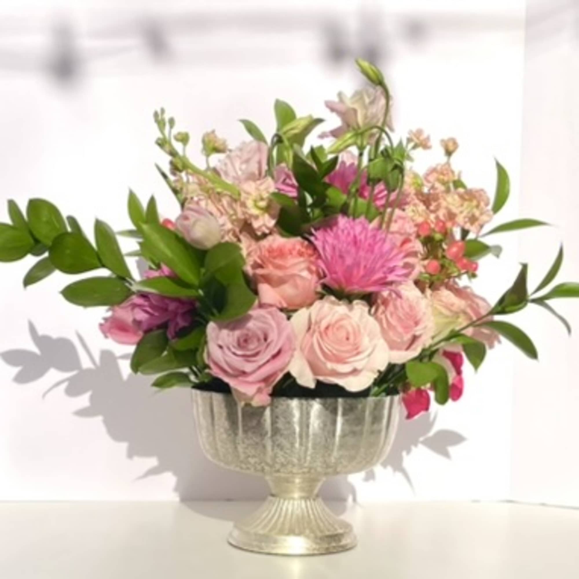 This arrangement bursts out of its container with pink tones from hot