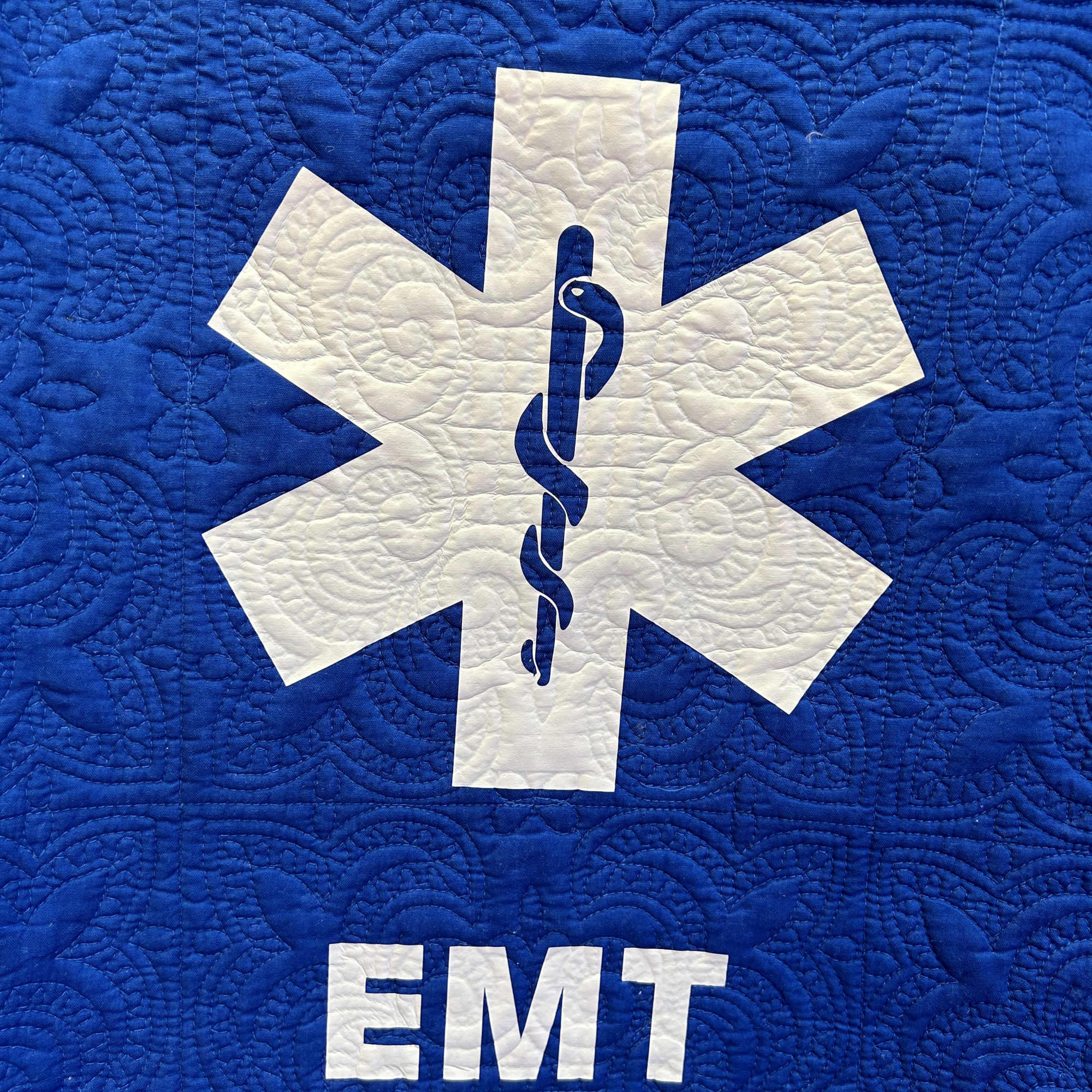 A 50" x 60" throw quilt with white EMT symbol on a A 50" x 60" throw quilt with white EMT symbol on a