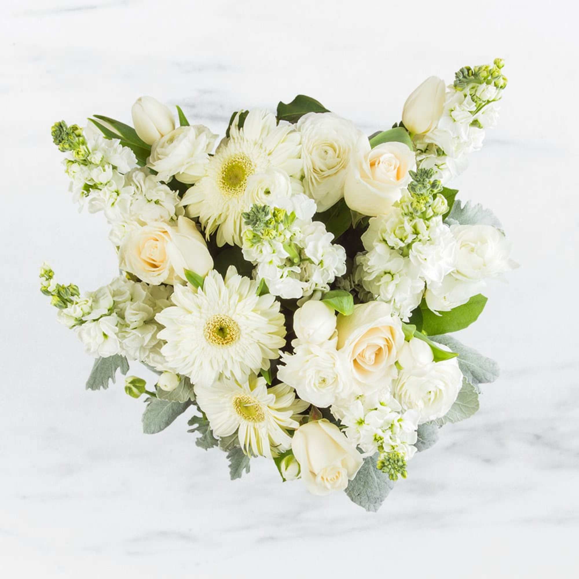 This arrangement contains gerbera daisies, roses, tulips, stock, and other seasonal blooms. This arrangement contains gerbera daisies, roses, tulips, stock, and other seasonal blooms.