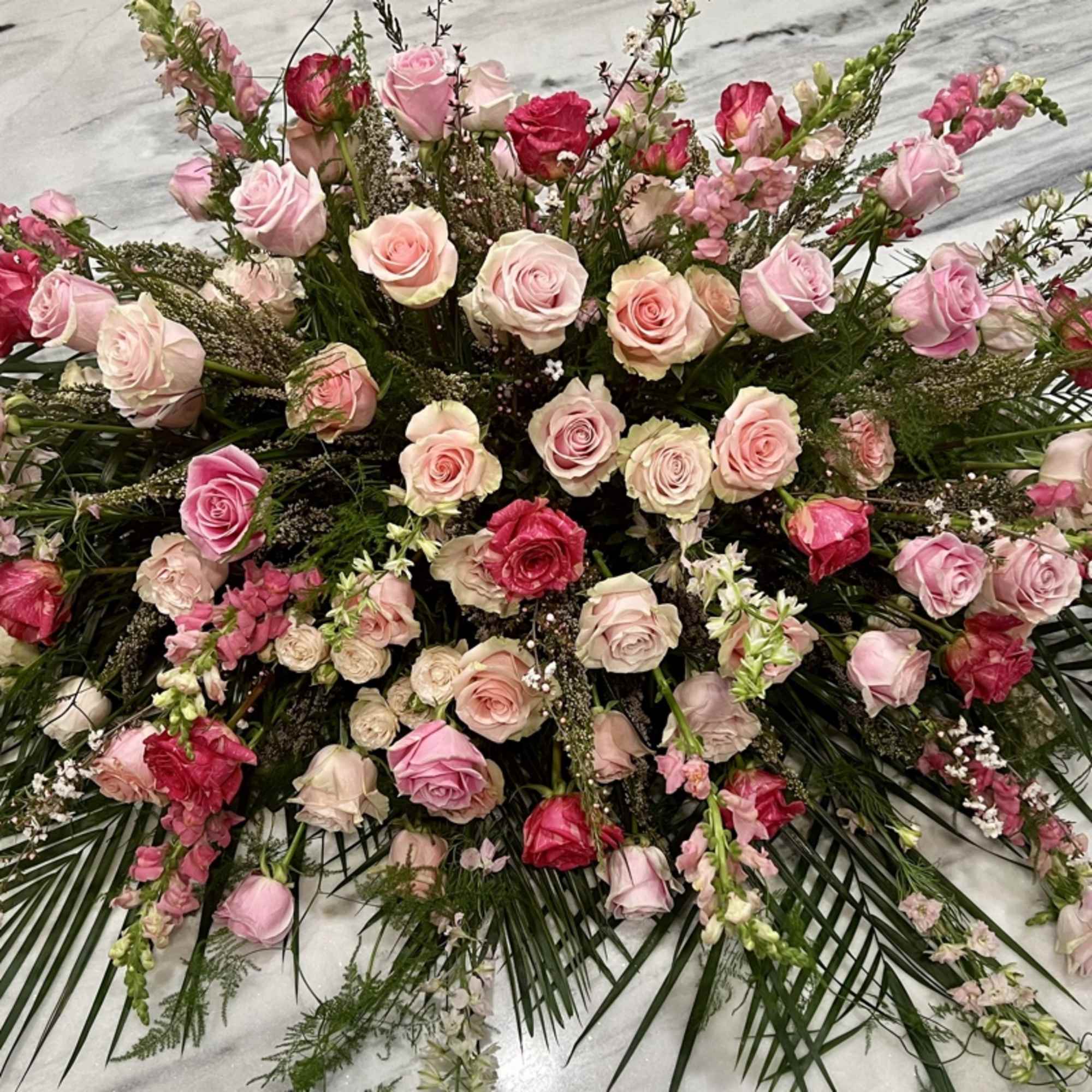Roses, lilies, and more come together for a blushing pink half casket