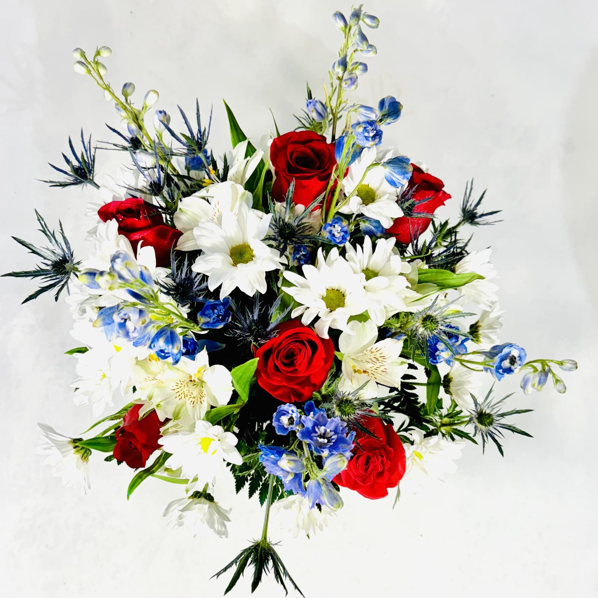 White daisies, red roses, white alstromeria, blue delphinium and thistle makes this