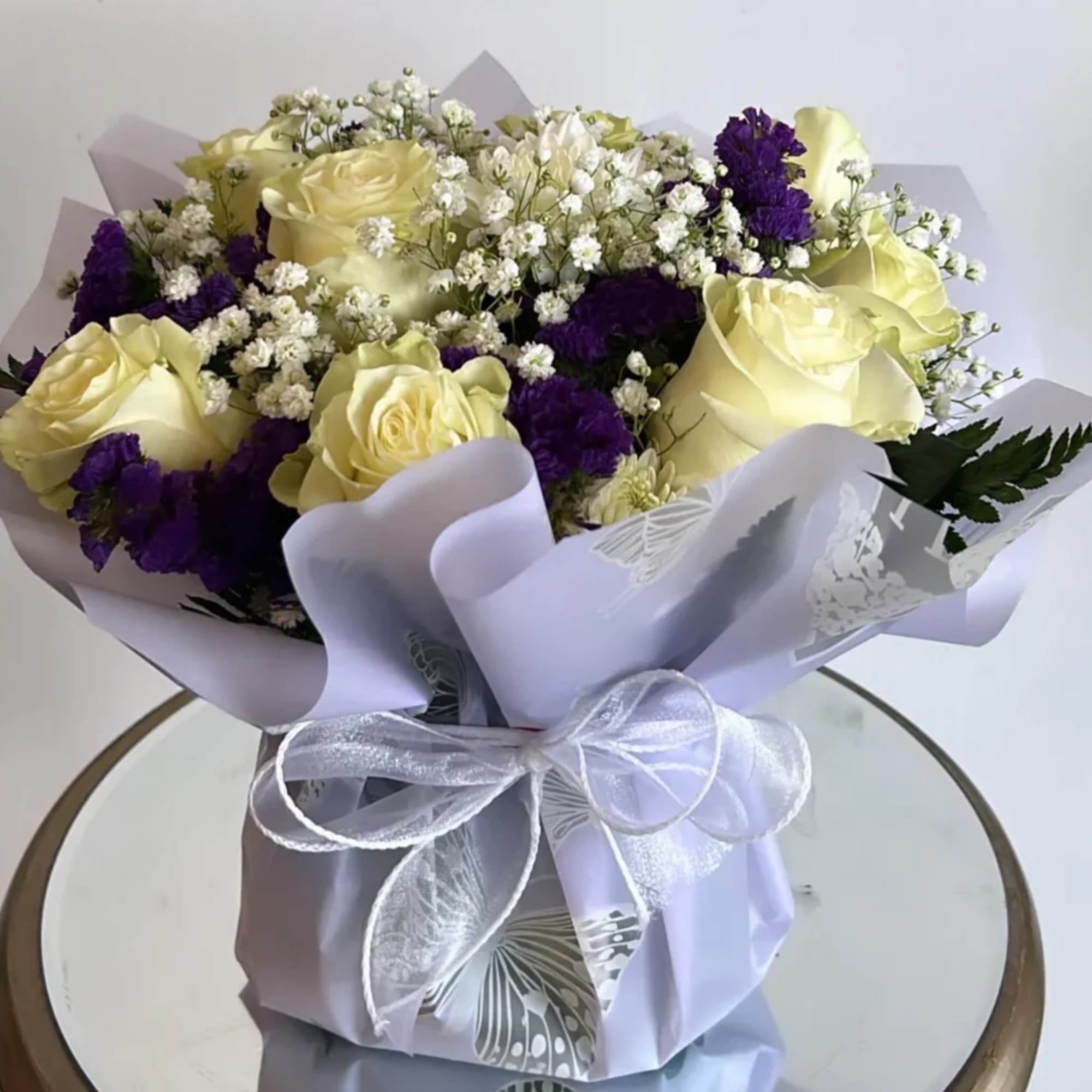 -The bouquet is composed primarily of delicate white roses, purple statice and -The bouquet is composed primarily of delicate white roses, purple statice and