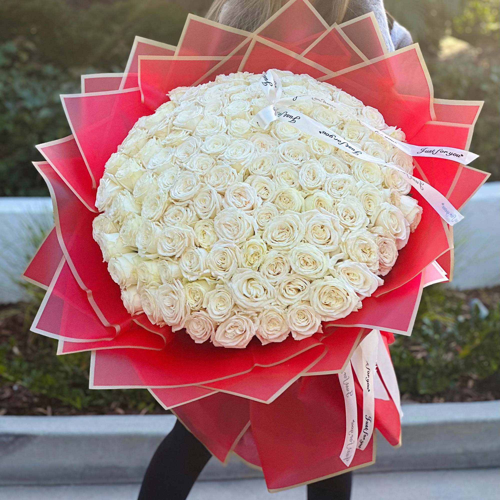 A bouquet of 100 pristine white roses, cradled in vibrant red wrapping