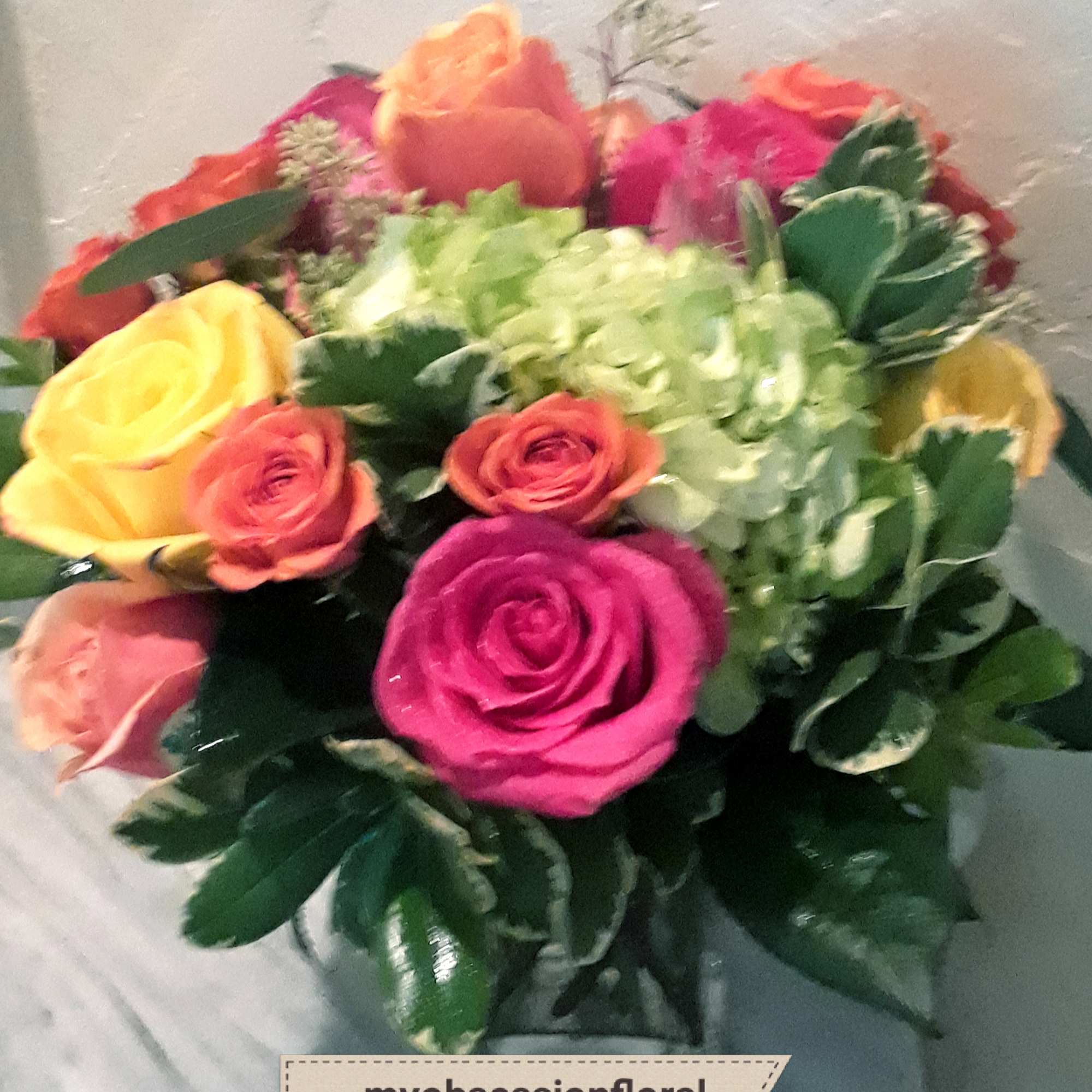 Pink, yellow and orange roses come together with green hydrangea for a