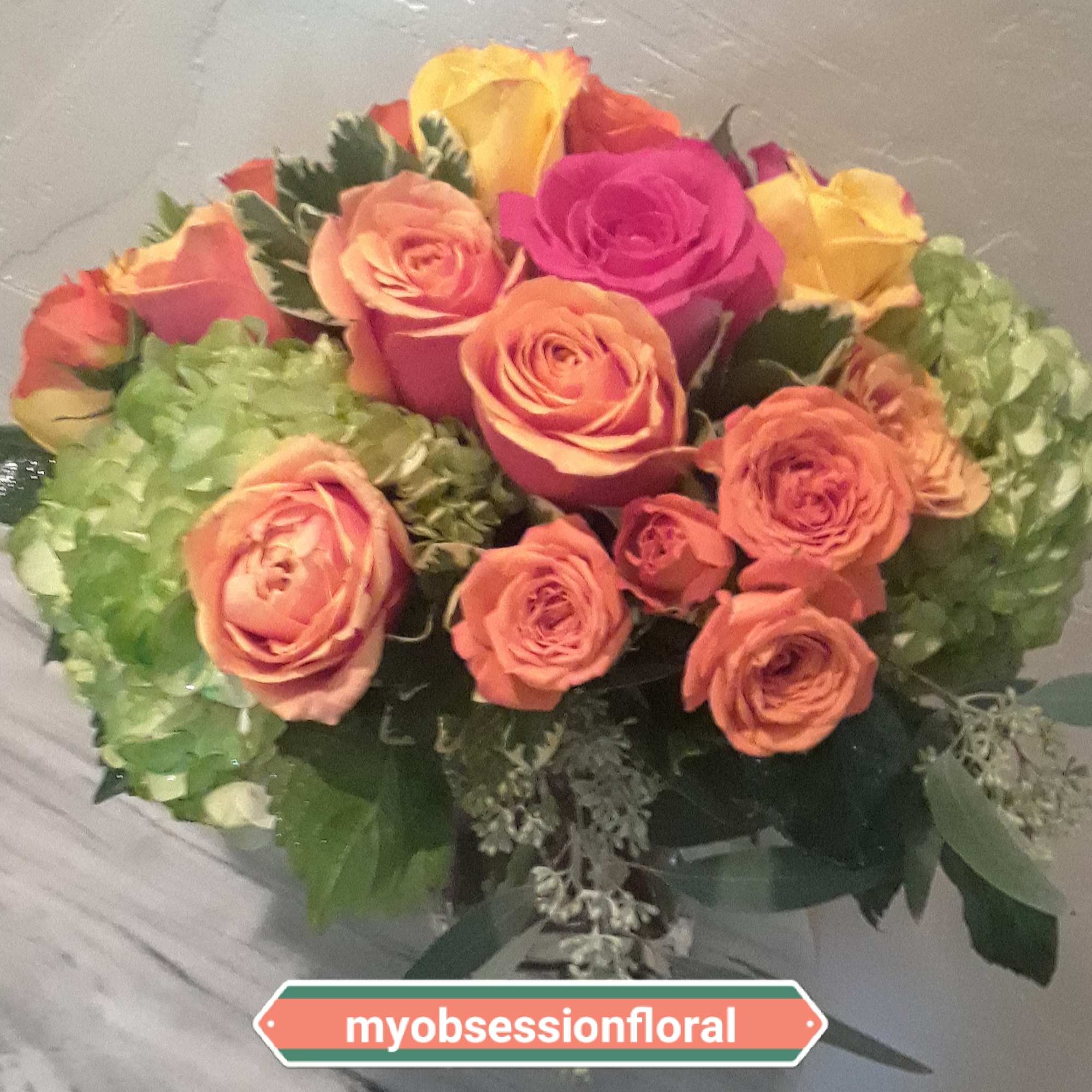 Pink, yellow and orange roses come together with green hydrangea for a