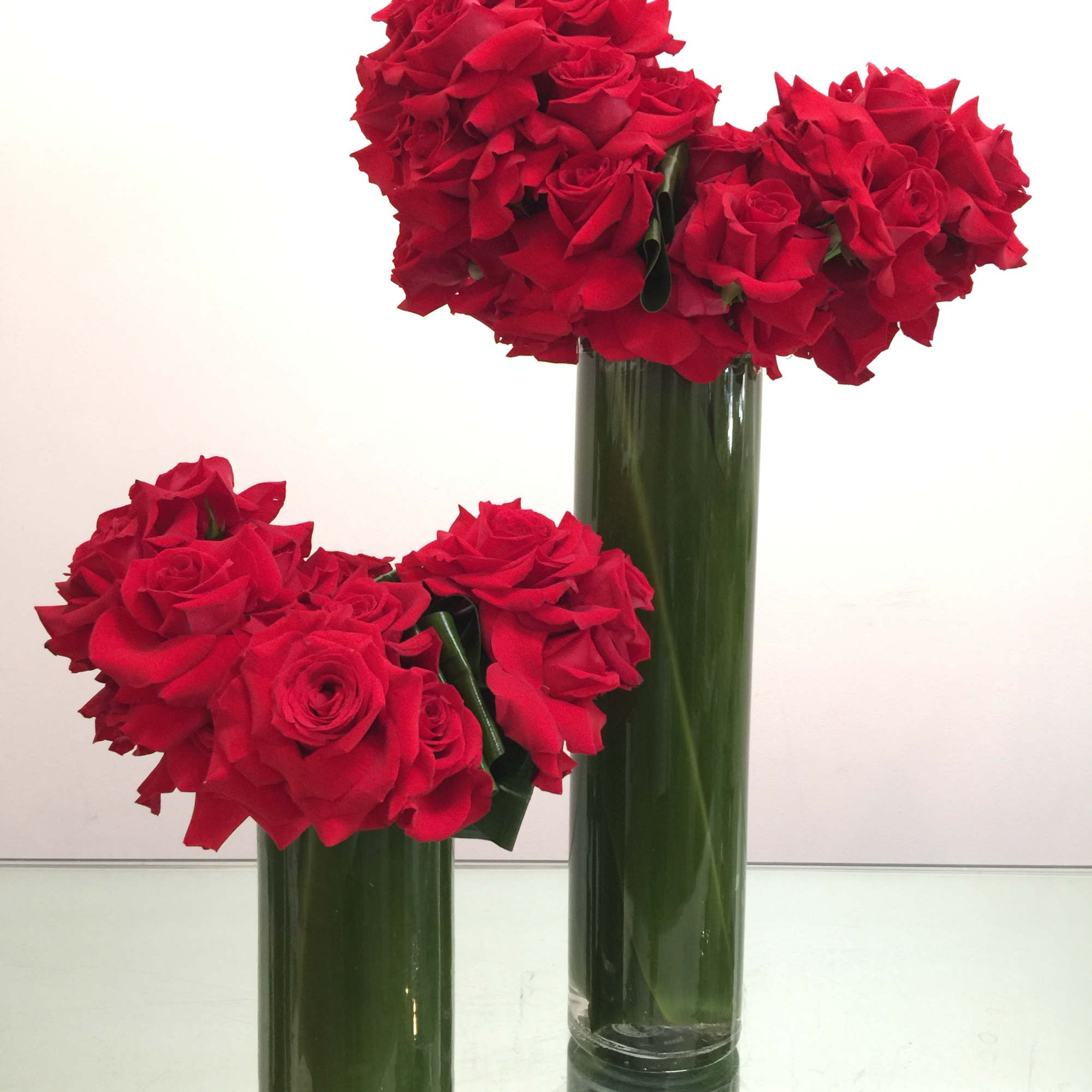 Two chic towers of red roses in leaf-lined cylinder vases. This contemporary