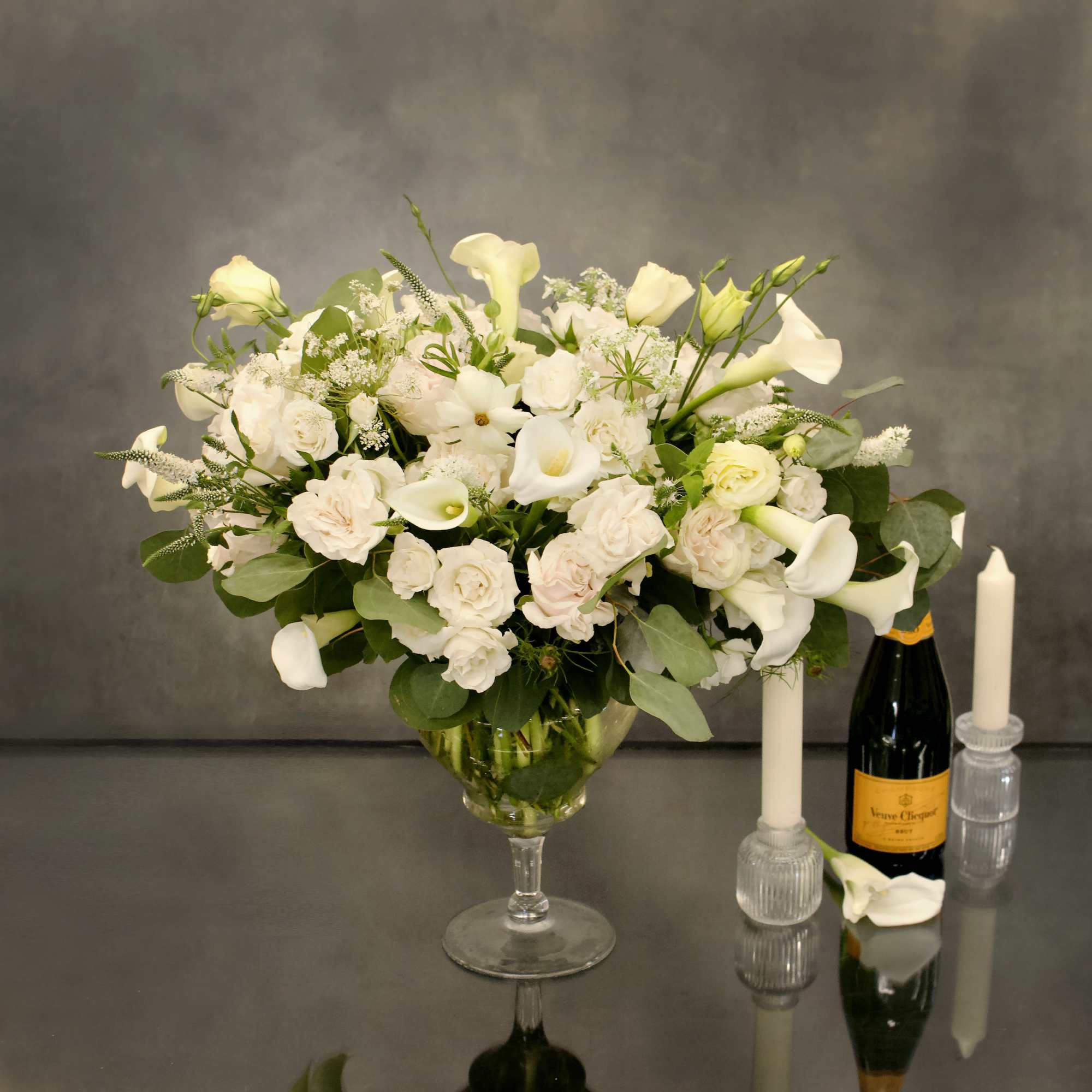 Pedestal glass vase with cream roses, calla lillies, and other complimentary floral.
Contemplate