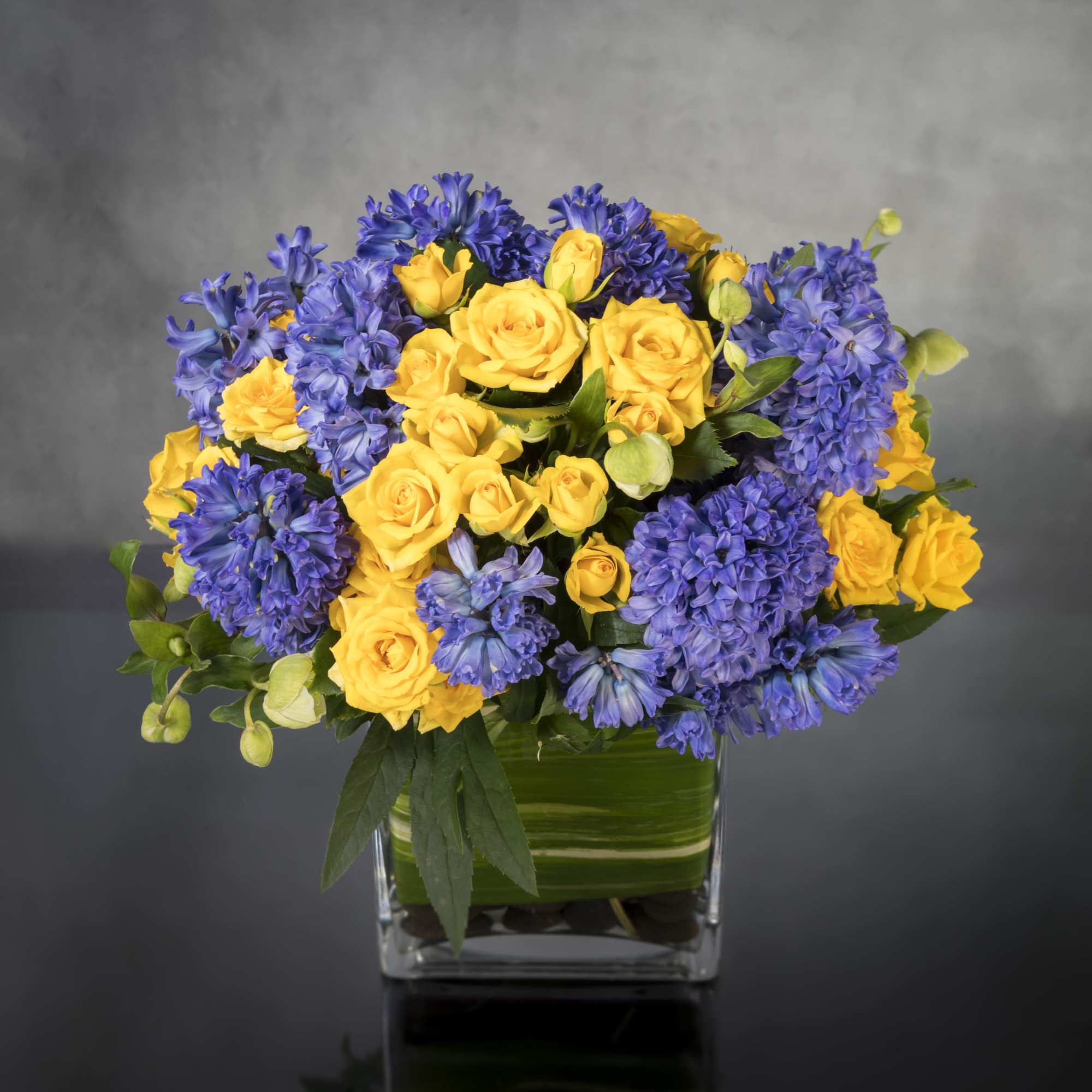 Summer Solstice features yellow spray Roses and purple Hyacinths, and seasonal flowers