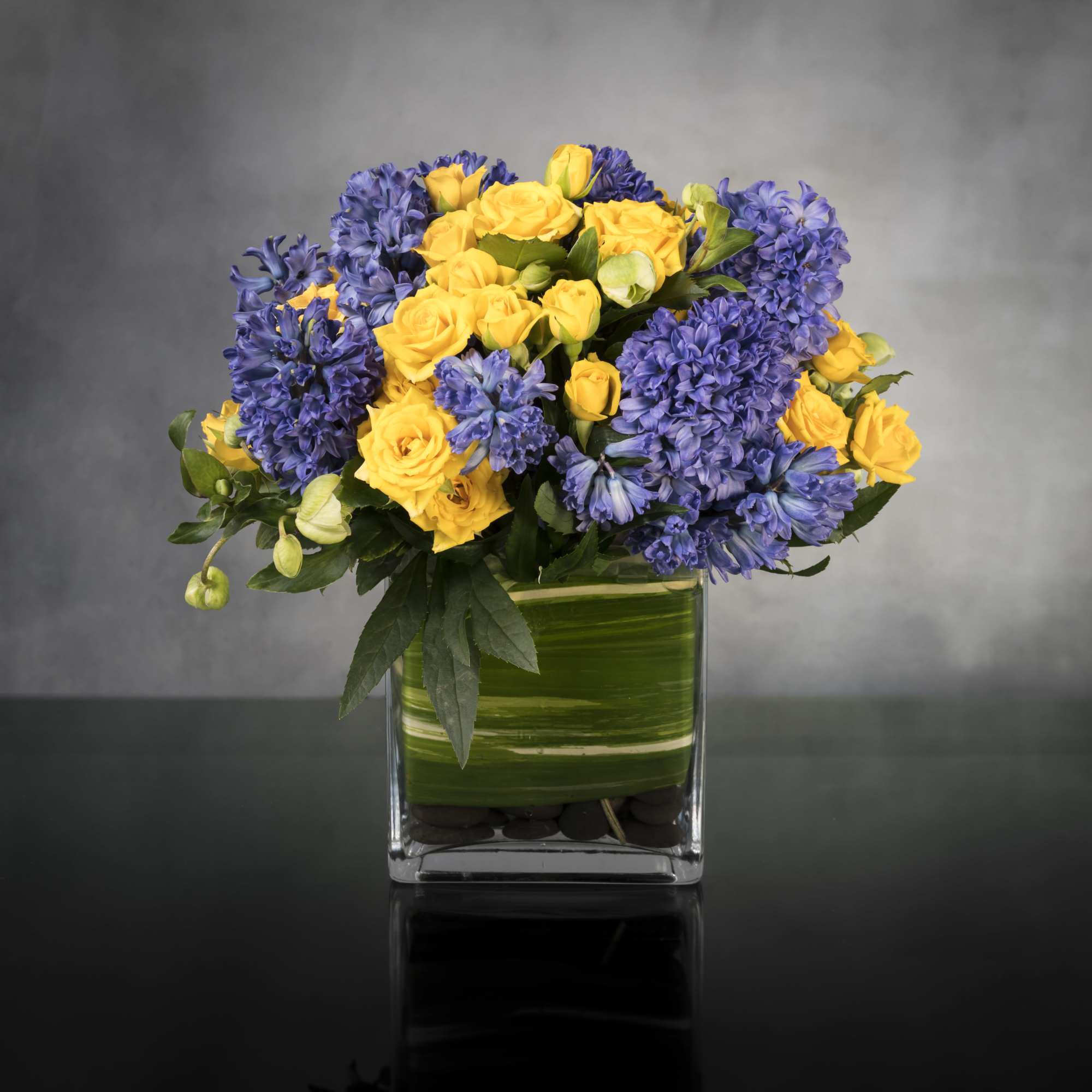 Summer Solstice features yellow spray Roses and purple Hyacinths, and seasonal flowers