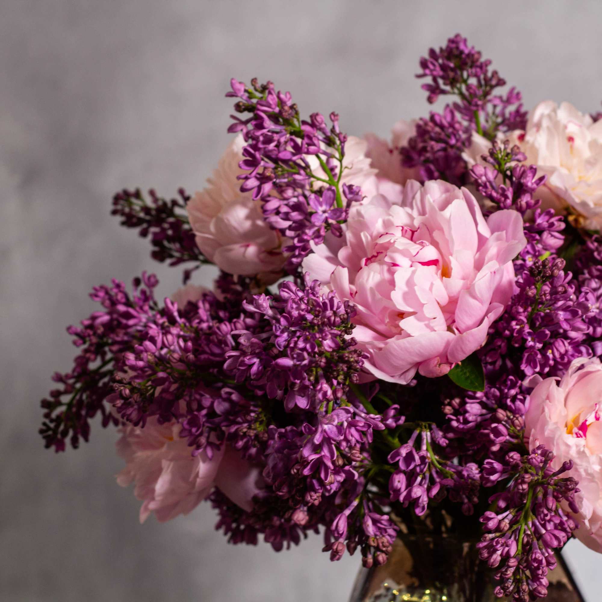 The beautiful arrangement features blush color peonies and purple lilacs gathered together