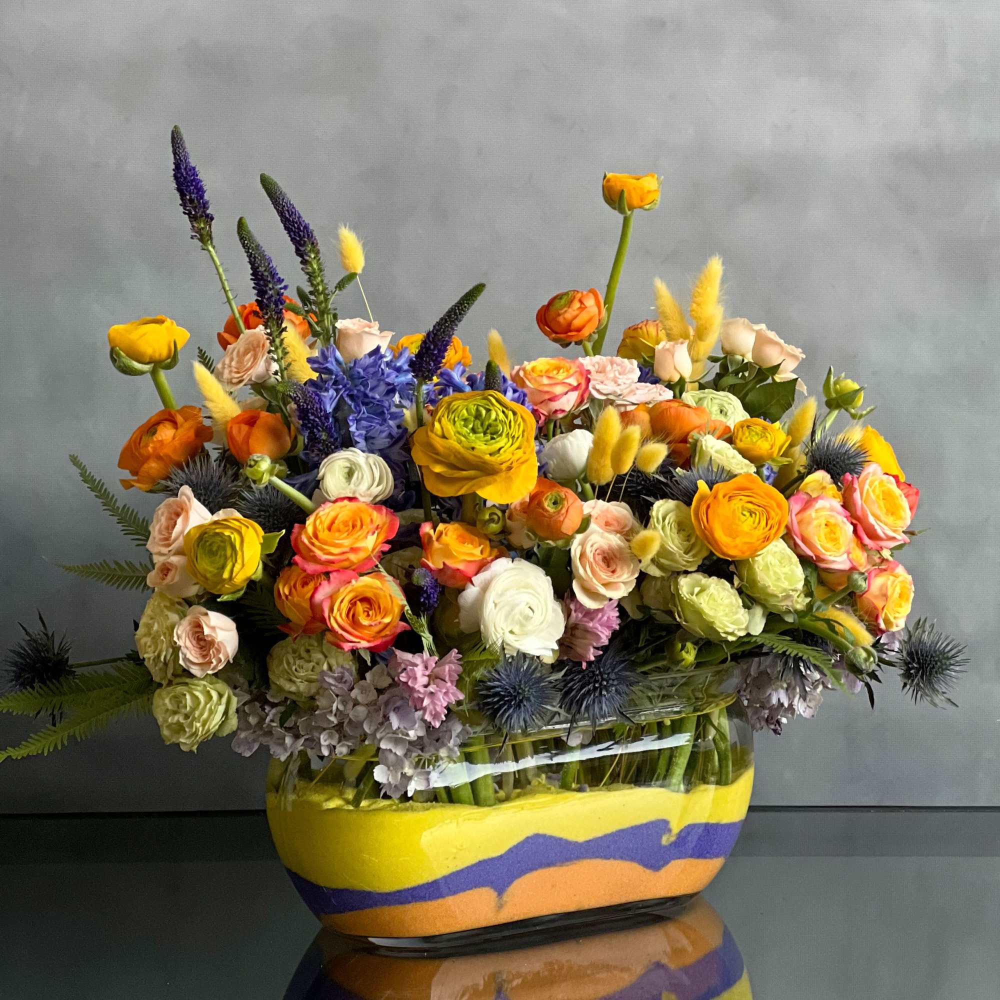 The design features elegant splashes of yellow ranunculus, orange, peach and white