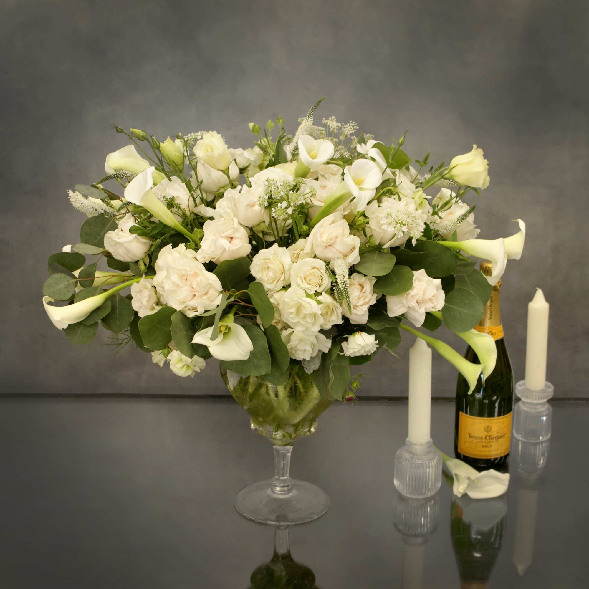 Pedestal glass vase with cream roses, calla lillies, and other complimentary floral.
Contemplate