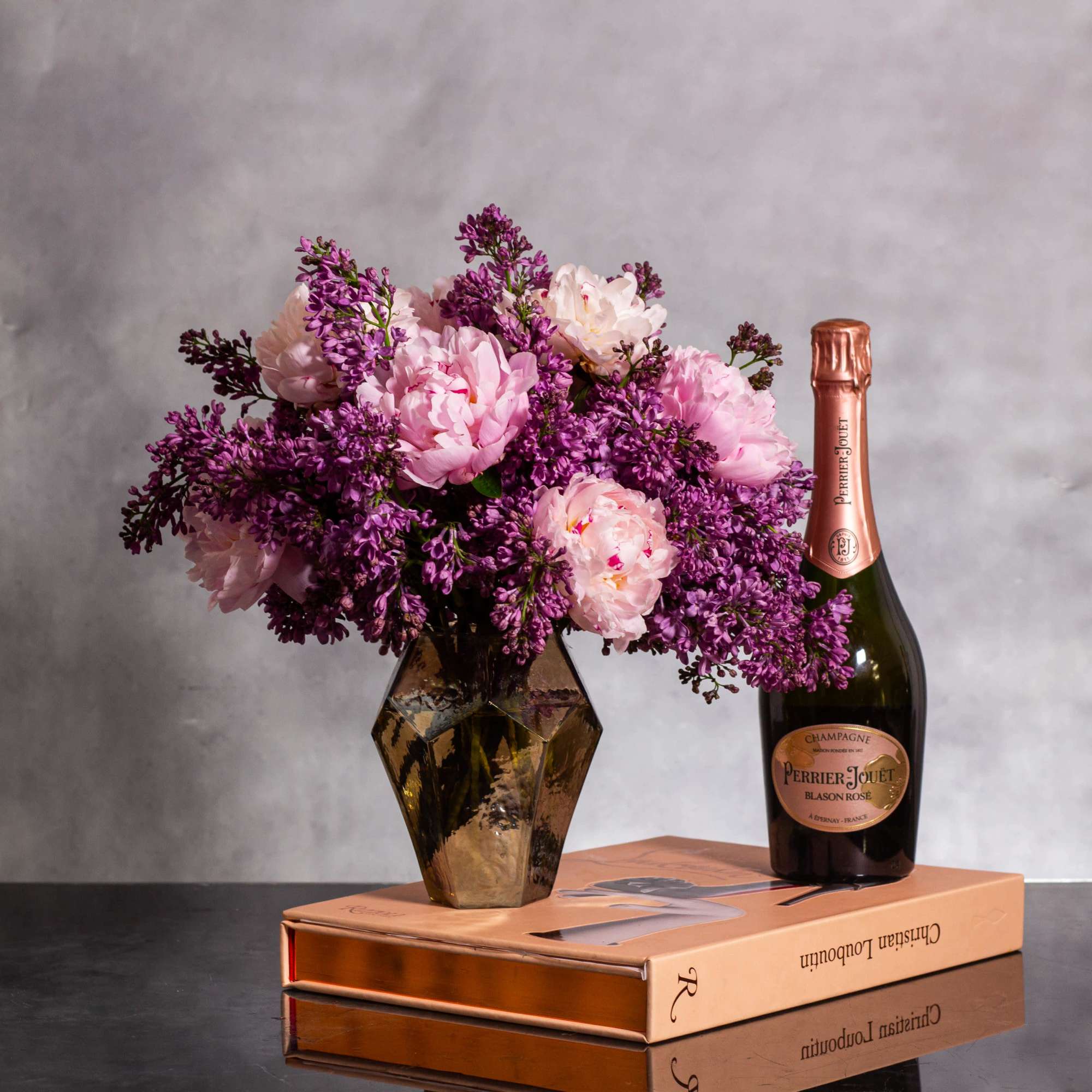 The beautiful arrangement features blush color peonies and purple lilacs gathered together